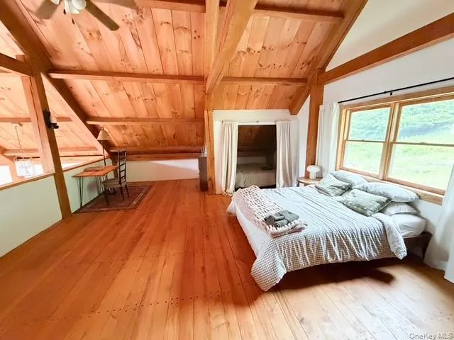 Vaulted ceiling with exposed wood beams, natural wood-finish flooring, and a ceiling fan Vaulted ceiling with exposed wood beams, natural wood-finish flooring, and a ceiling fan