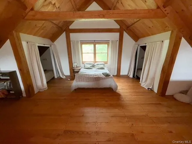 Spacious attic room featuring exposed wooden beams and rich wood-finish flooring Spacious attic room featuring exposed wooden beams and rich wood-finish flooring