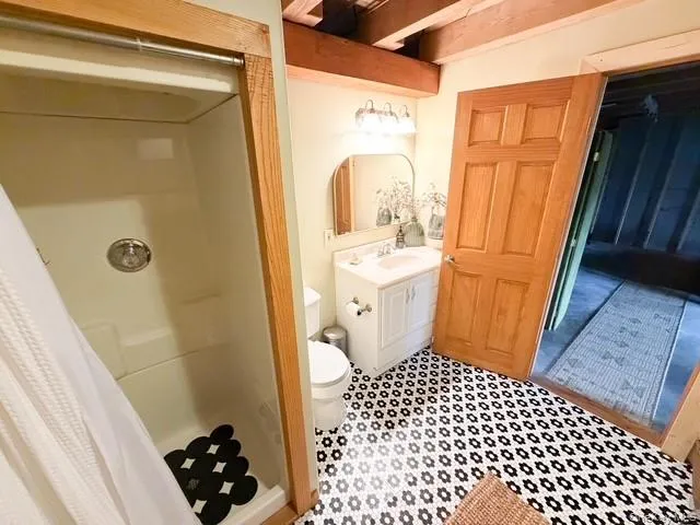 Bathroom featuring patterned floor tiles, a single vanity with a white countertop, and exposed ceiling beams Bathroom featuring patterned floor tiles, a single vanity with a white countertop, and exposed ceiling beams