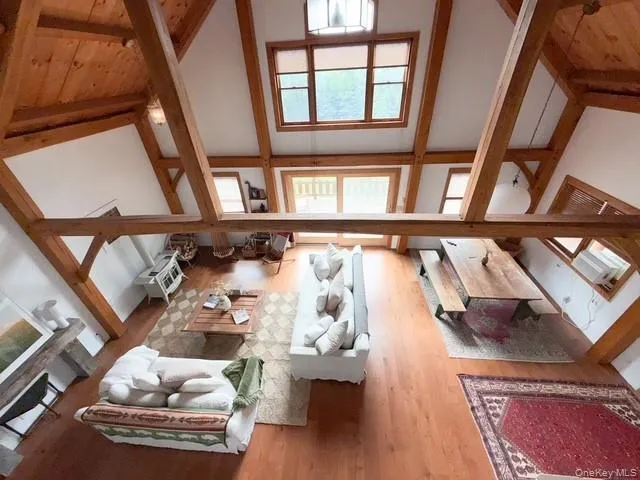 Expansive open-concept room featuring vaulted ceilings with exposed timber beams, hardwood flooring, and multiple windows Expansive open-concept room featuring vaulted ceilings with exposed timber beams, hardwood flooring, and multiple windows