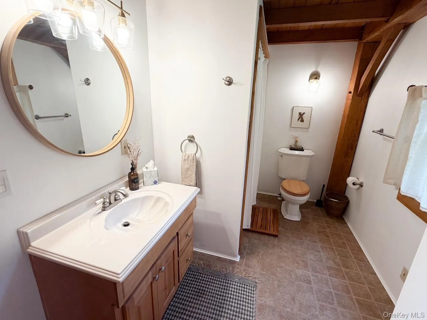 Bathroom featuring a wood-finish vanity with an integrated sink, a large round mirror, and a three-light vanity fixture Bathroom featuring a wood-finish vanity with an integrated sink, a large round mirror, and a three-light vanity fixture