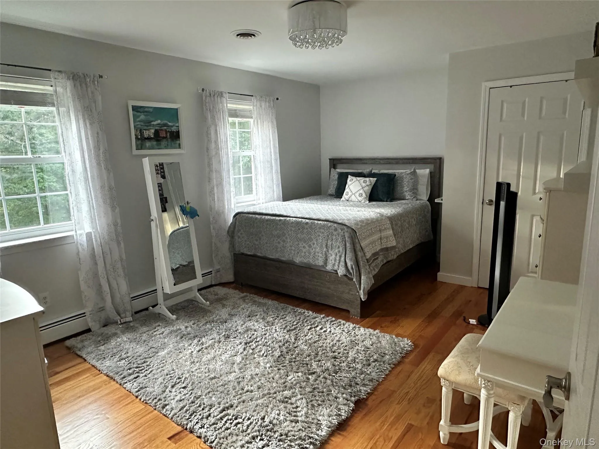 Hardwood flooring throughout this second bedroom featuring a ceiling-mounted light fixture, two windows, and a paneled door Hardwood flooring throughout this second bedroom featuring a ceiling-mounted light fixture, two windows, and a paneled door