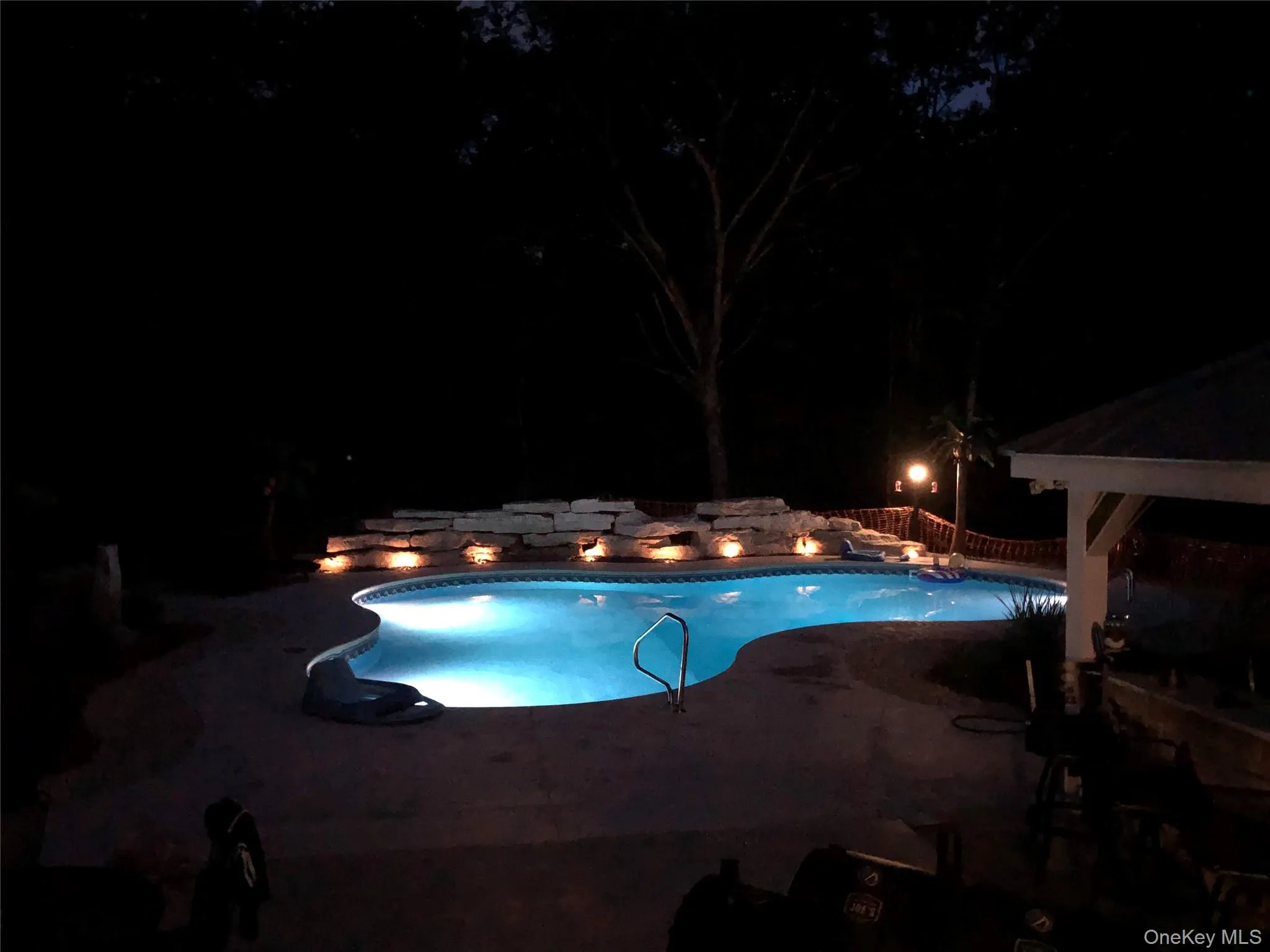 Freeform swimming pool with integrated lighting, natural stone rockery, and surrounding hardscaping Freeform swimming pool with integrated lighting, natural stone rockery, and surrounding hardscaping