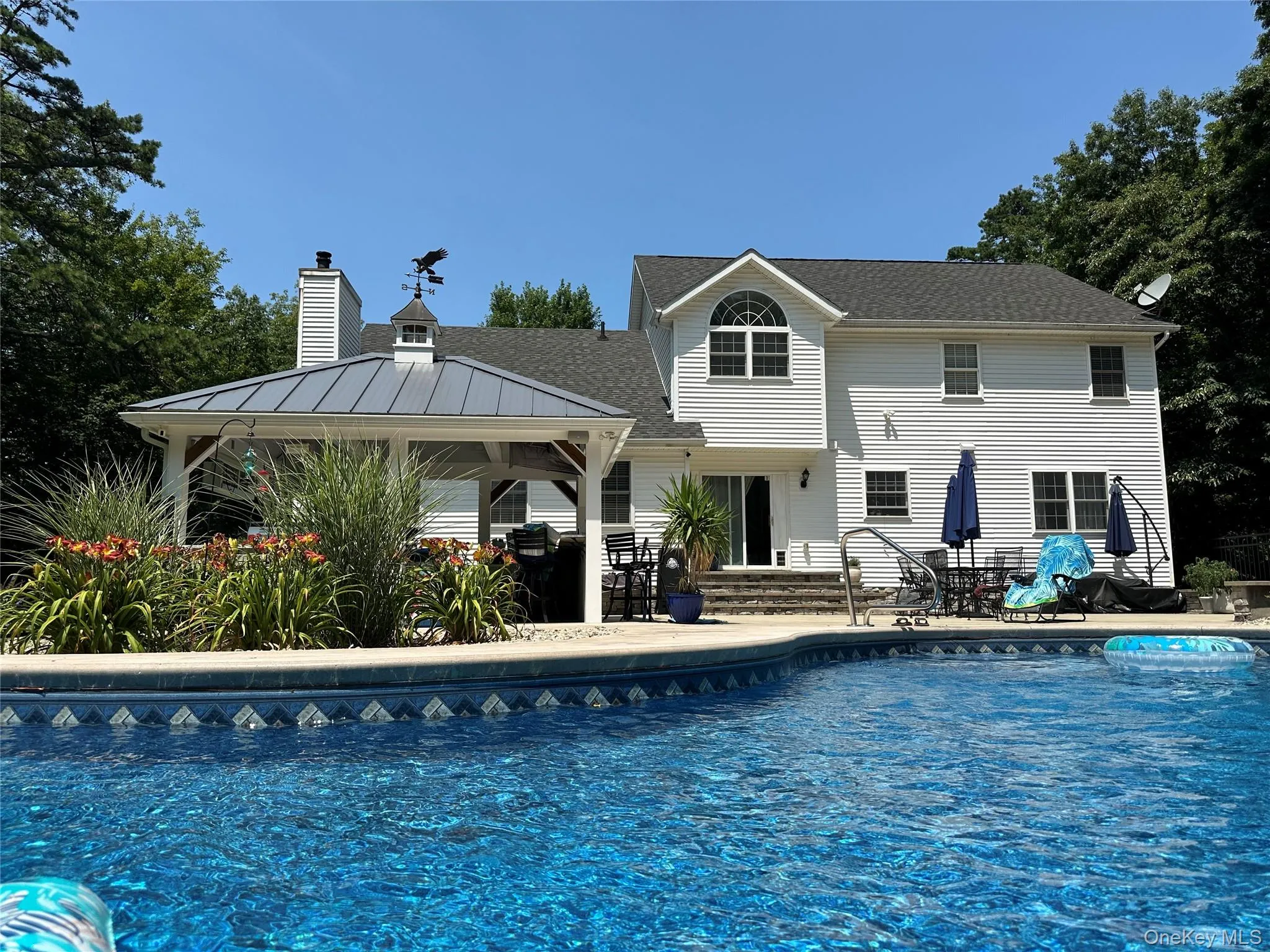 Expansive backyard featuring a built-in salt water swimming pool with tile accents, a covered pavilion with a metal roof, and a stone patio area Expansive backyard featuring a built-in salt water swimming pool with tile accents, a covered pavilion with a metal roof, and a stone patio area