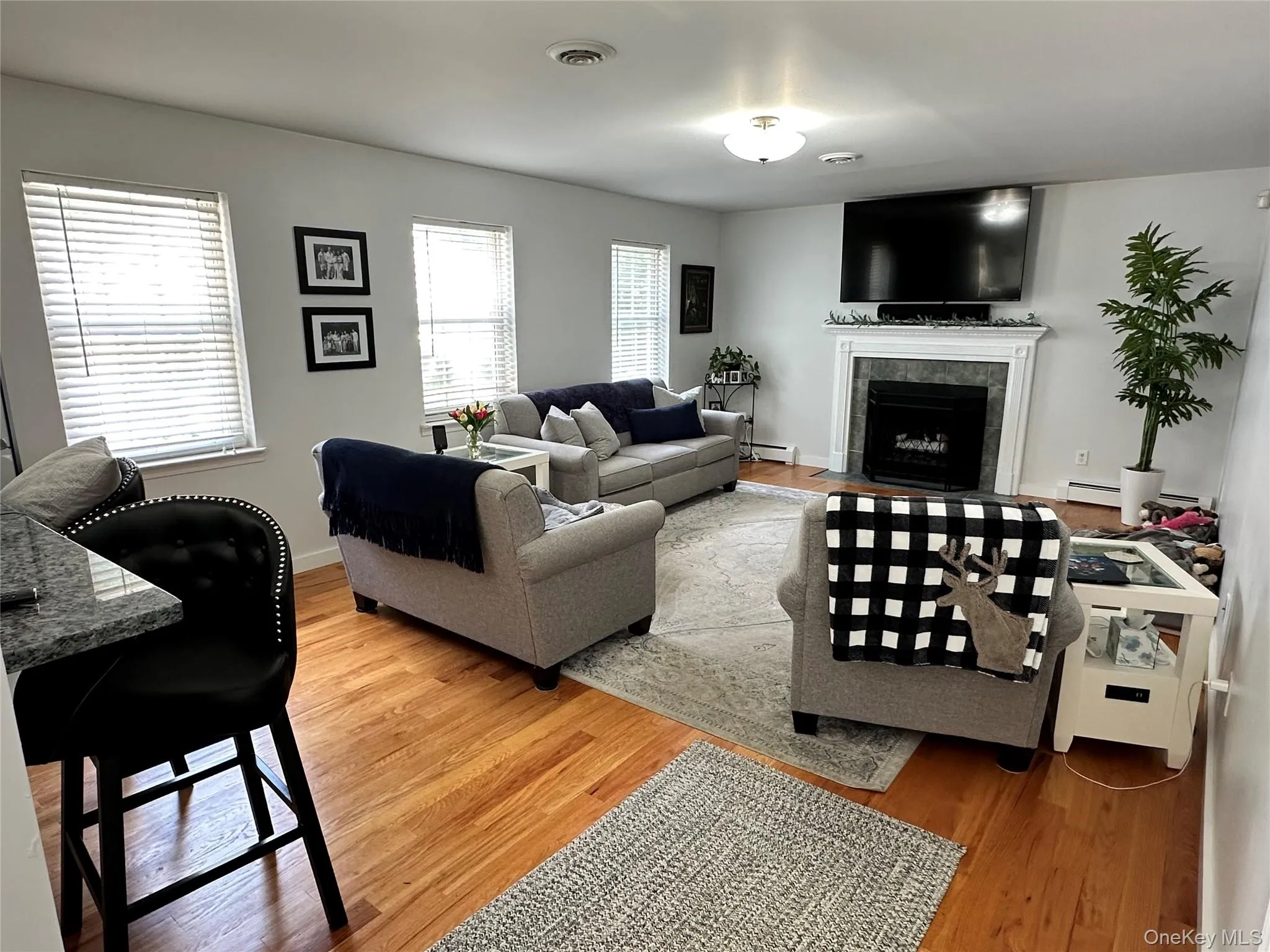 Living area featuring wood-finish flooring, a fireplace with a decorative mantel, and multiple windows with blinds Living area featuring wood-finish flooring, a fireplace with a decorative mantel, and multiple windows with blinds