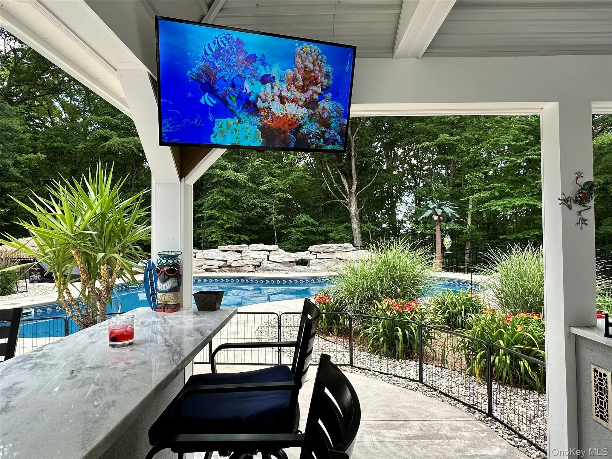 Outdoor covered patio featuring a built-in bar with a light-toned countertop, integrated television, and pool views Outdoor covered patio featuring a built-in bar with a light-toned countertop, integrated television, and pool views