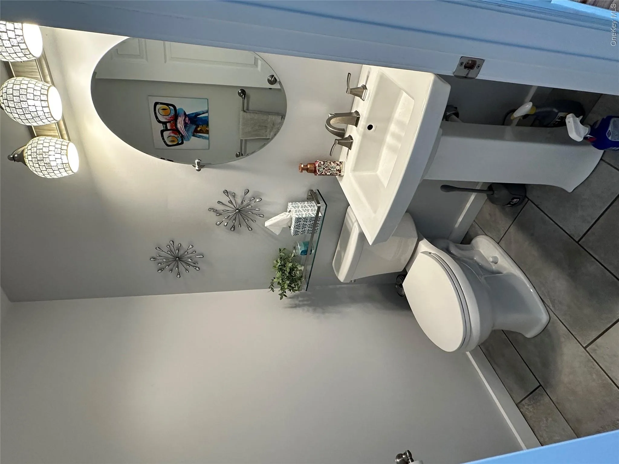 Half Bathroom on main level featuring a pedestal sink, brushed nickel faucet, large round mirror, and tile flooring Half Bathroom on main level featuring a pedestal sink, brushed nickel faucet, large round mirror, and tile flooring