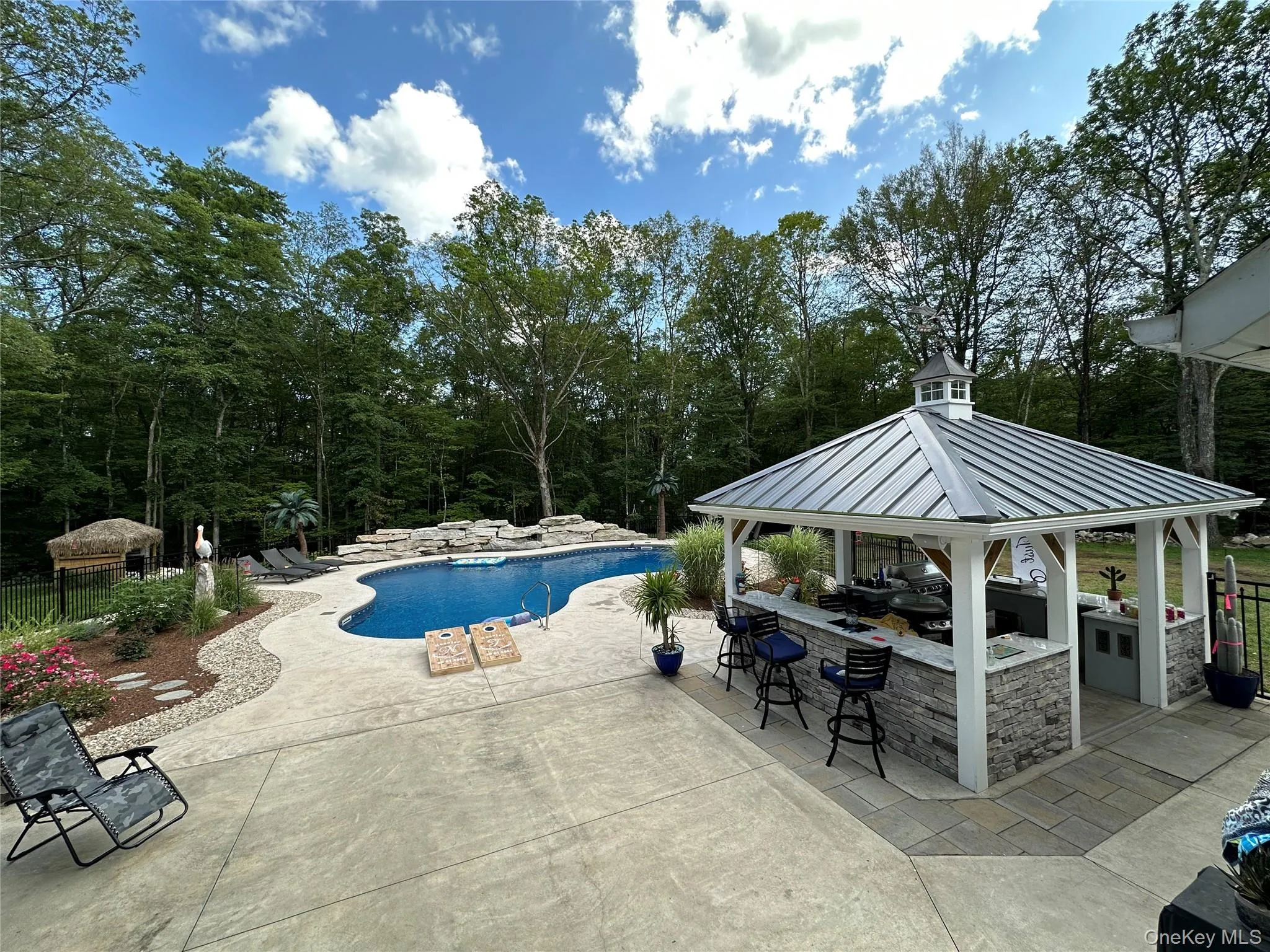 Expansive outdoor living area featuring a freeform swimming pool with rock features, a stamped concrete patio, and mature trees Expansive outdoor living area featuring a freeform swimming pool with rock features, a stamped concrete patio, and mature trees
