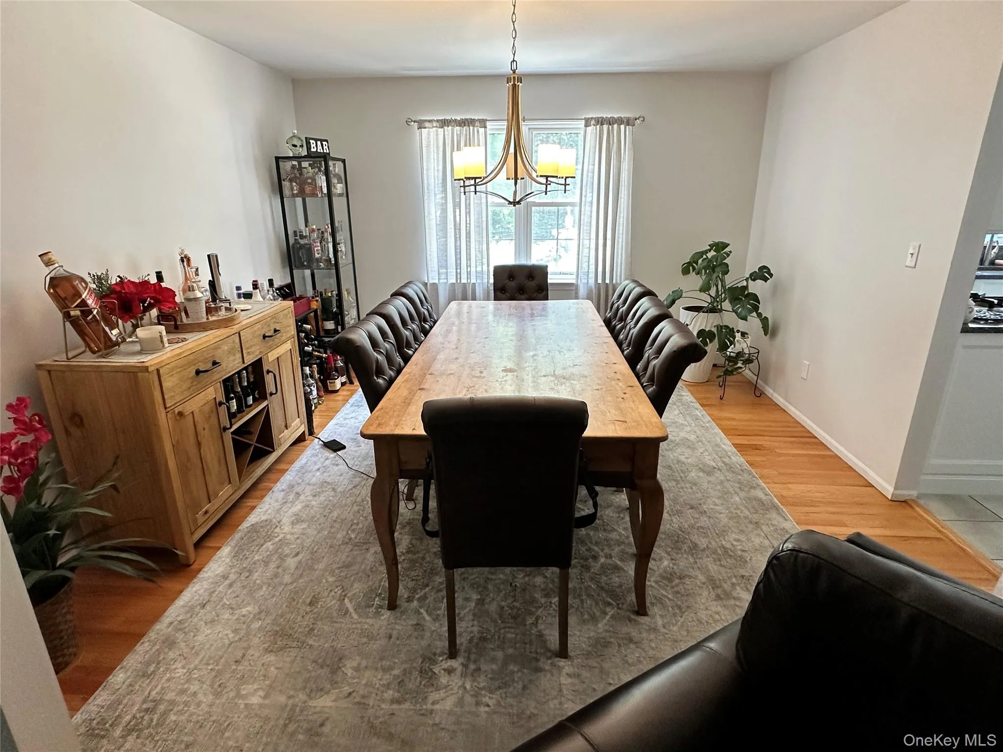 Spacious dining area featuring hardwood flooring, a large window with privacy blinds, and a central chandelier Spacious dining area featuring hardwood flooring, a large window with privacy blinds, and a central chandelier