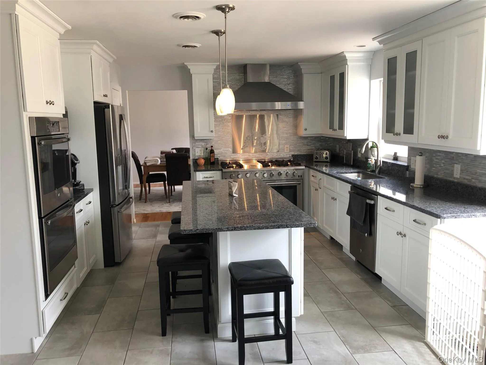 Kitchen featuring an island with seating, white shaker cabinetry, stainless steel appliances, granite countertops, and a tiled backsplash Kitchen featuring an island with seating, white shaker cabinetry, stainless steel appliances, granite countertops, and a tiled backsplash