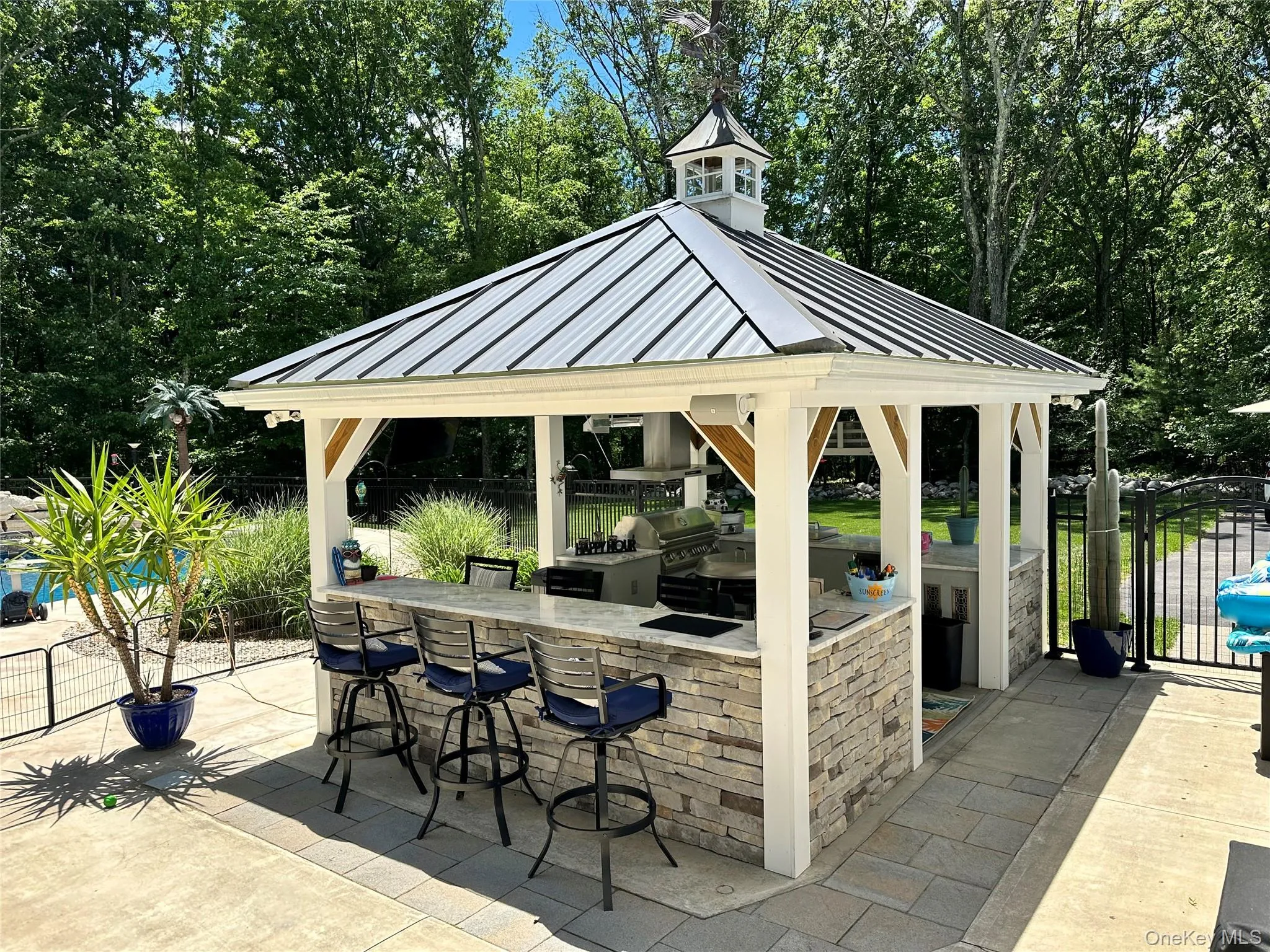 Outdoor kitchen gazebo featuring a metal roof with a cupola, stone veneer base, granite countertop, and integrated grilling station Outdoor kitchen gazebo featuring a metal roof with a cupola, stone veneer base, granite countertop, and integrated grilling station