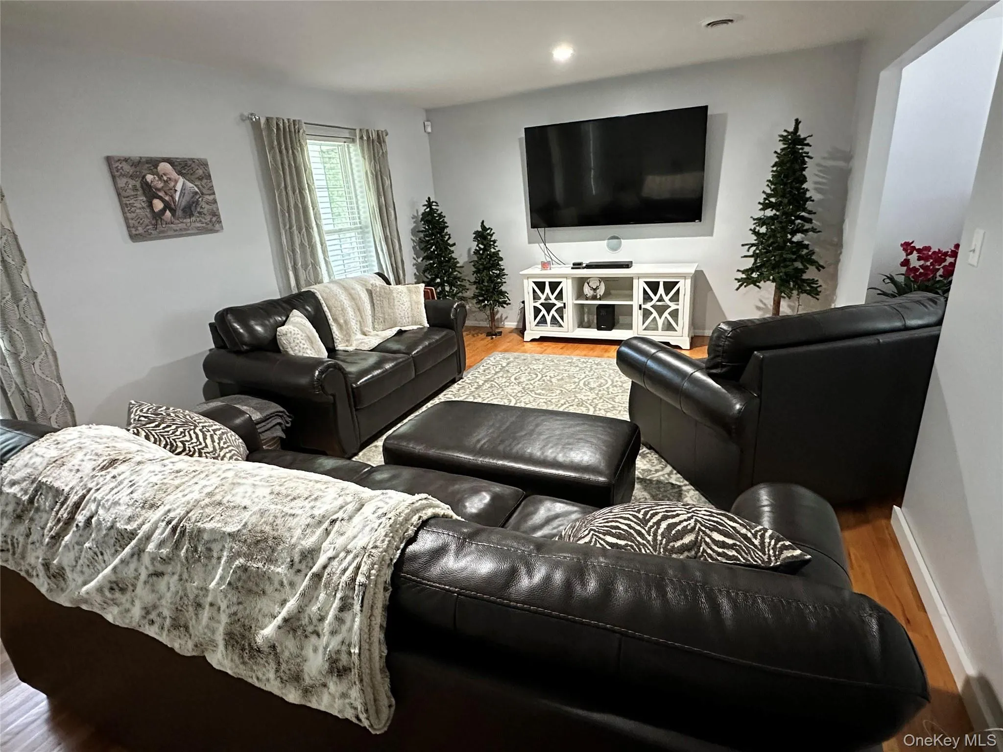 Spacious living area featuring light-toned wall paint and wood-finish flooring Spacious living area featuring light-toned wall paint and wood-finish flooring