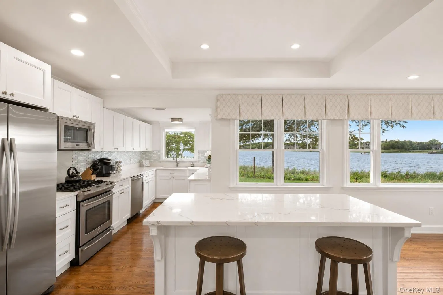 Kitchen featuring white shaker cabinetry, stainless steel appliances, and a mosaic tile backsplash Kitchen featuring white shaker cabinetry, stainless steel appliances, and a mosaic tile backsplash