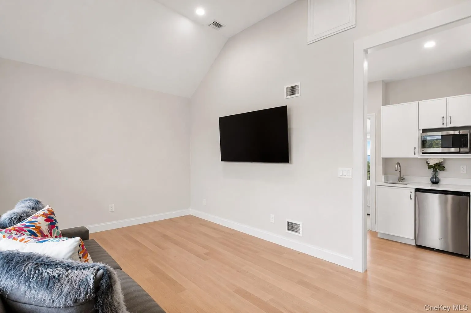 Vaulted ceiling with recessed lighting, wood-finish flooring, and a wall-mounted television Vaulted ceiling with recessed lighting, wood-finish flooring, and a wall-mounted television