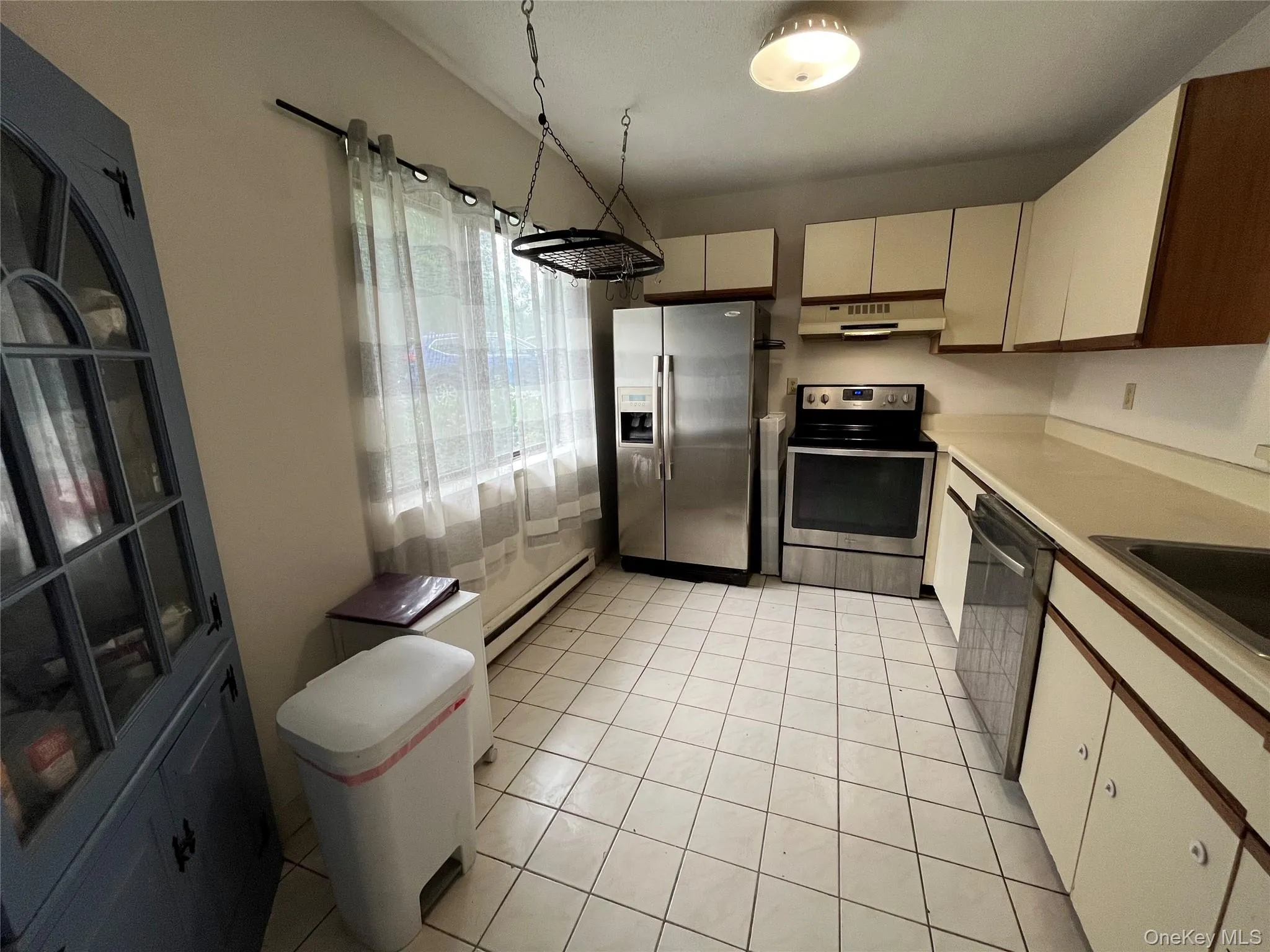 Kitchen featuring stainless steel appliances, under cabinet range hood, baseboard heating, light countertops, and light tile patterned floors Kitchen featuring stainless steel appliances, under cabinet range hood, baseboard heating, light countertops, and light tile patterned floors