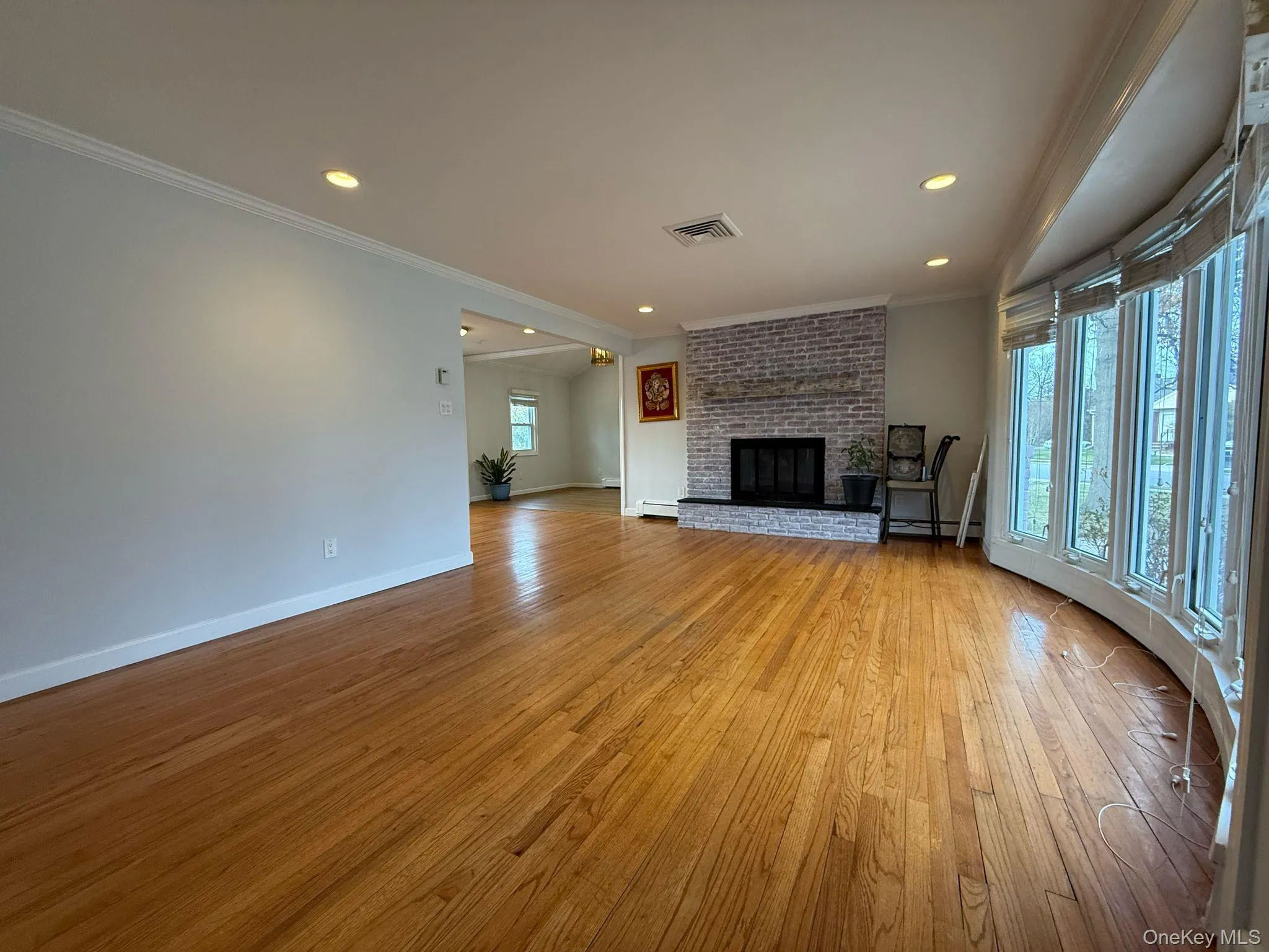 Unfurnished living room with crown molding, a brick fireplace, light wood-style flooring, baseboards, and visible vents Unfurnished living room with crown molding, a brick fireplace, light wood-style flooring, baseboards, and visible vents