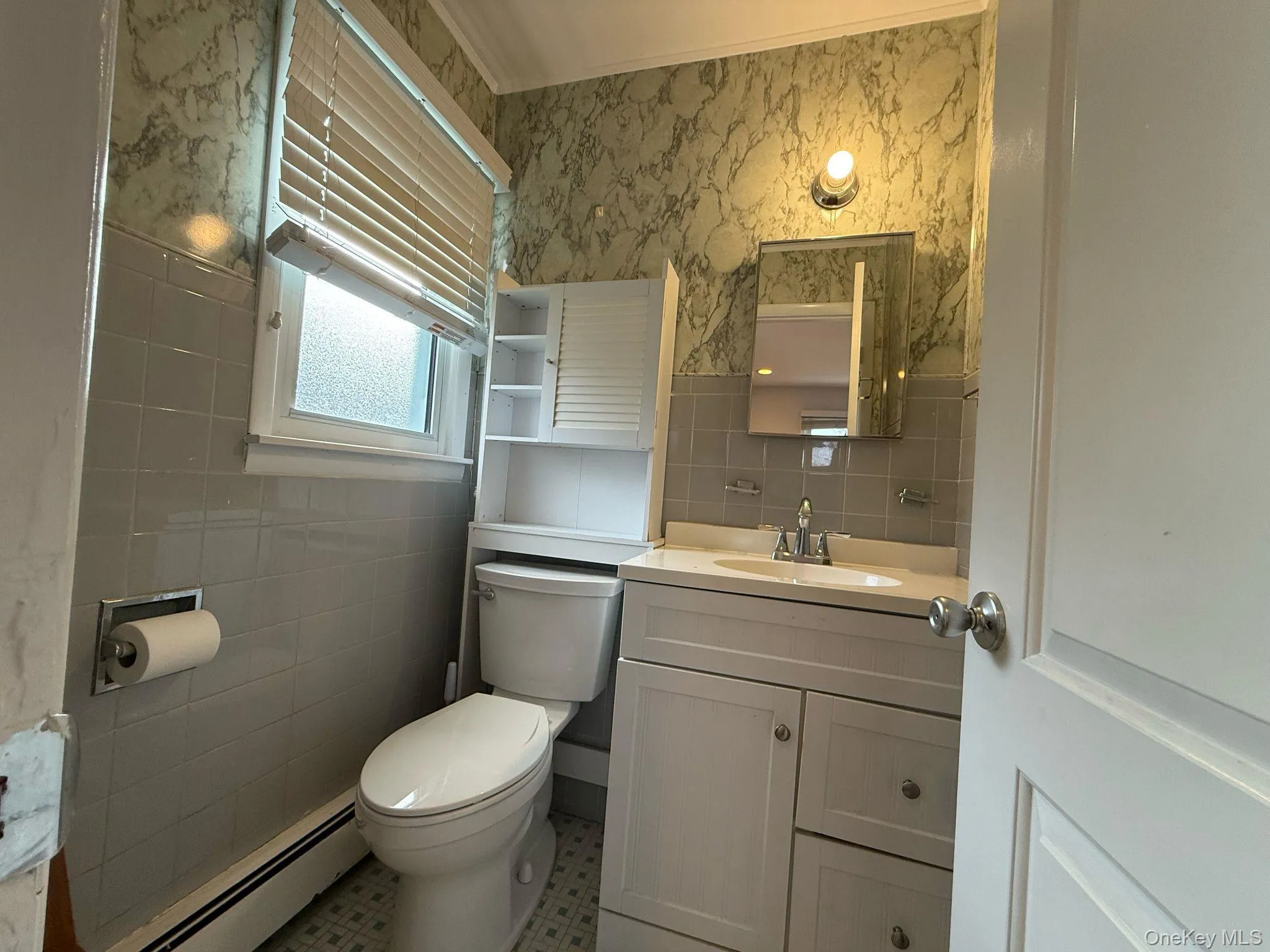 Bathroom featuring toilet, vanity, baseboard heating, wallpapered walls, and tile walls Bathroom featuring toilet, vanity, baseboard heating, wallpapered walls, and tile walls
