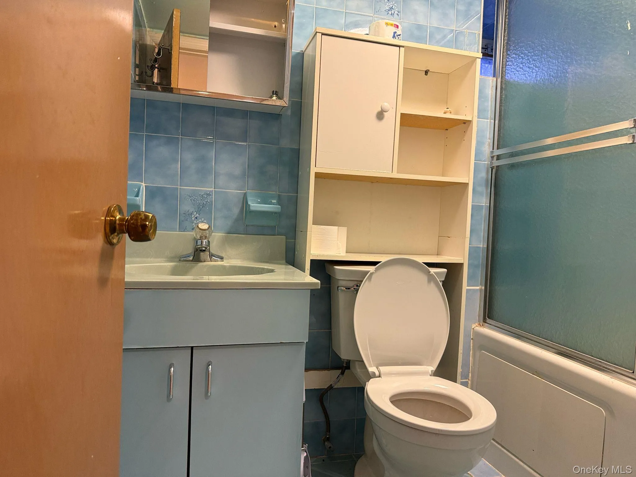 Bathroom featuring vanity, shower / bath combination with glass door, tile walls, toilet, and backsplash Bathroom featuring vanity, shower / bath combination with glass door, tile walls, toilet, and backsplash