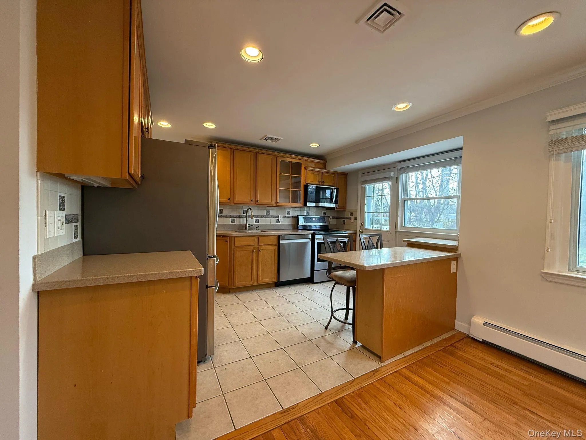 Kitchen with visible vents, ornamental molding, brown cabinets, stainless steel appliances, and baseboard heating Kitchen with visible vents, ornamental molding, brown cabinets, stainless steel appliances, and baseboard heating