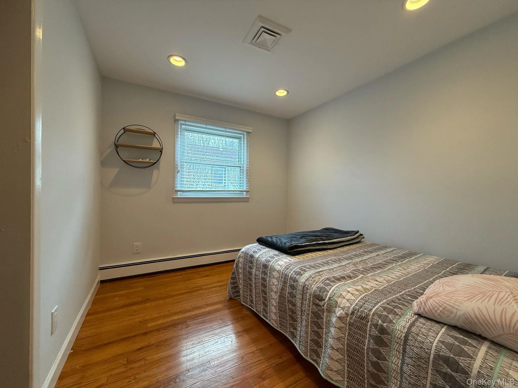 Bedroom featuring visible vents, hardwood / wood-style flooring, baseboards, recessed lighting, and a baseboard heating unit Bedroom featuring visible vents, hardwood / wood-style flooring, baseboards, recessed lighting, and a baseboard heating unit