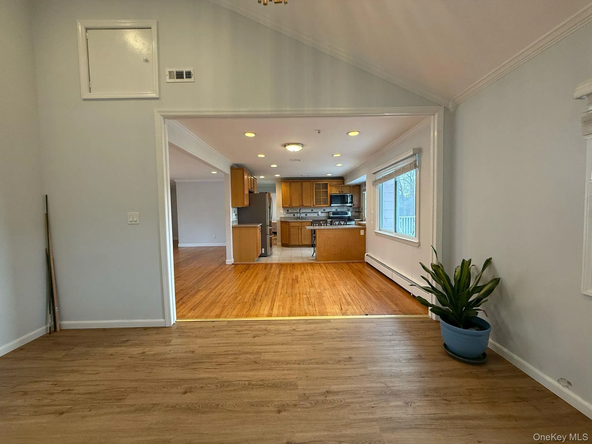 Kitchen with light wood-style floors, visible vents, a baseboard radiator, appliances with stainless steel finishes, and brown cabinetry Kitchen with light wood-style floors, visible vents, a baseboard radiator, appliances with stainless steel finishes, and brown cabinetry