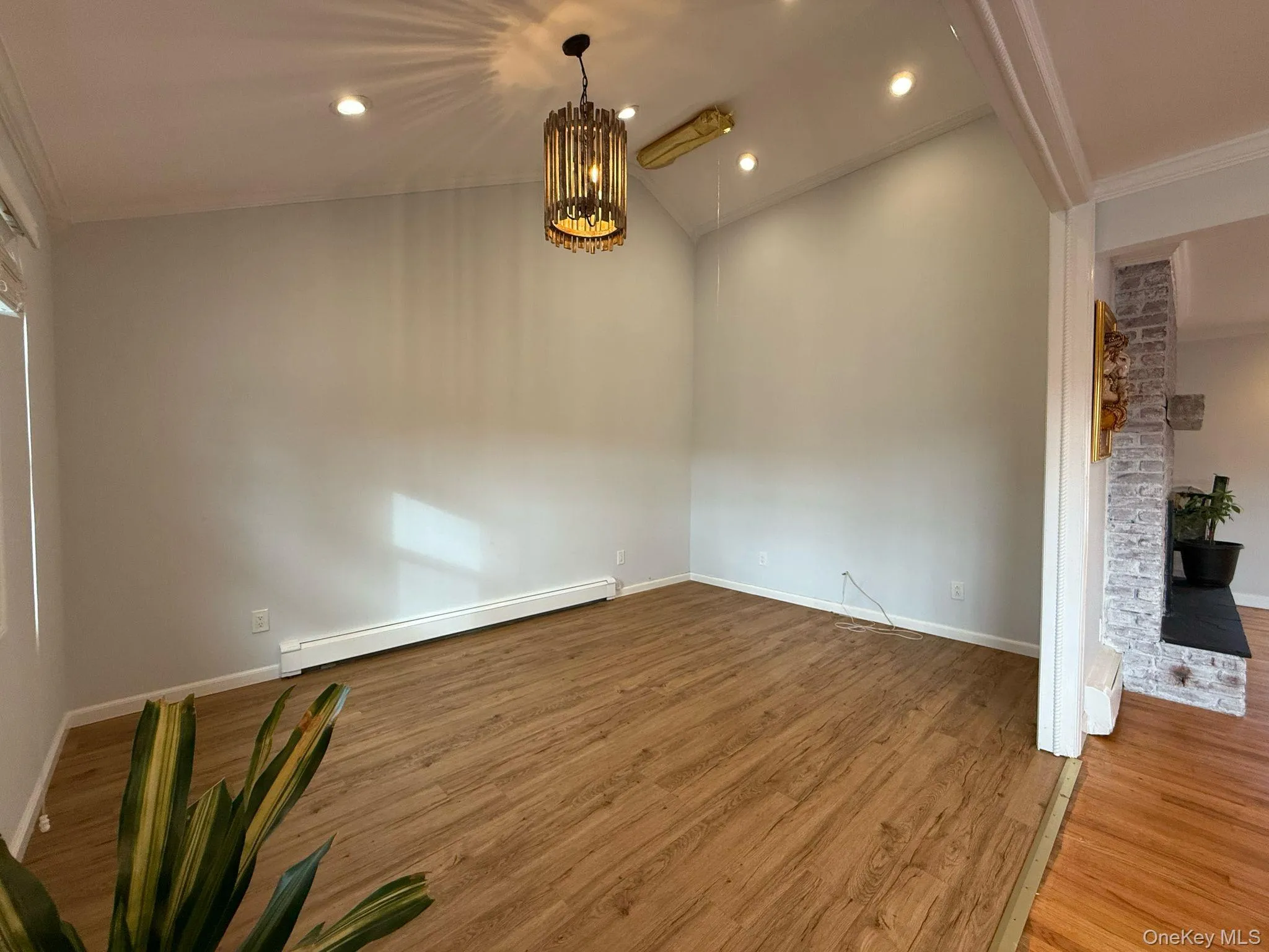Spare room with a baseboard radiator, baseboards, ornamental molding, wood finished floors, and a notable chandelier Spare room with a baseboard radiator, baseboards, ornamental molding, wood finished floors, and a notable chandelier