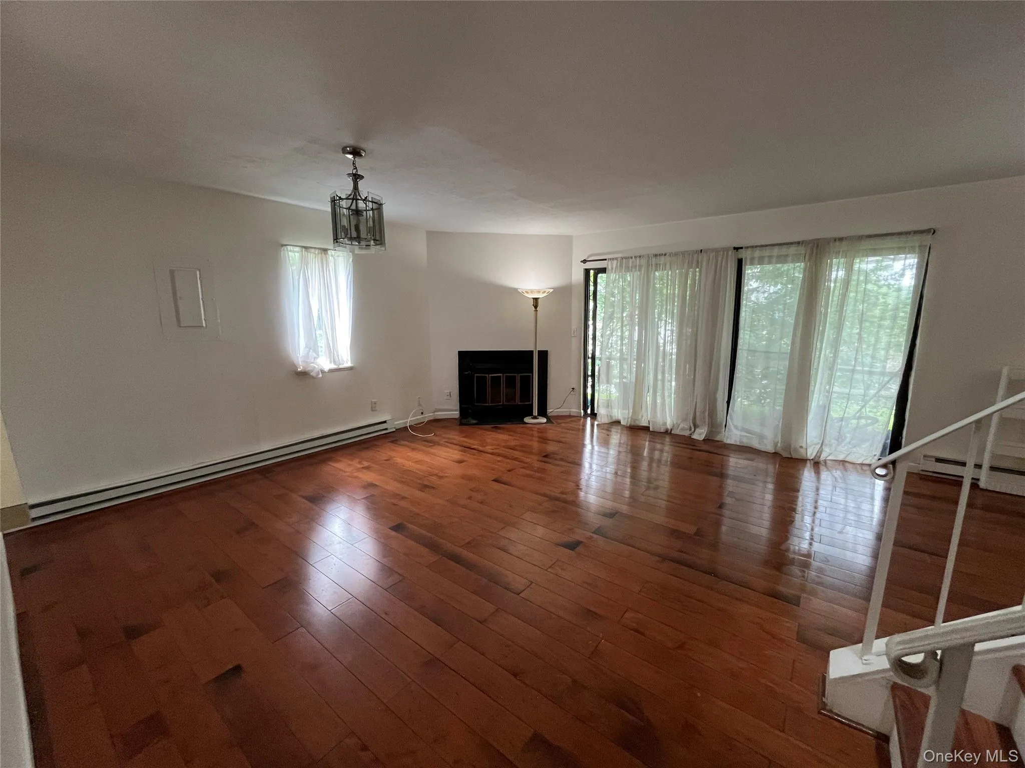 Unfurnished living room featuring a baseboard heating unit, plenty of natural light, a glass covered fireplace, and wood-type flooring Unfurnished living room featuring a baseboard heating unit, plenty of natural light, a glass covered fireplace, and wood-type flooring