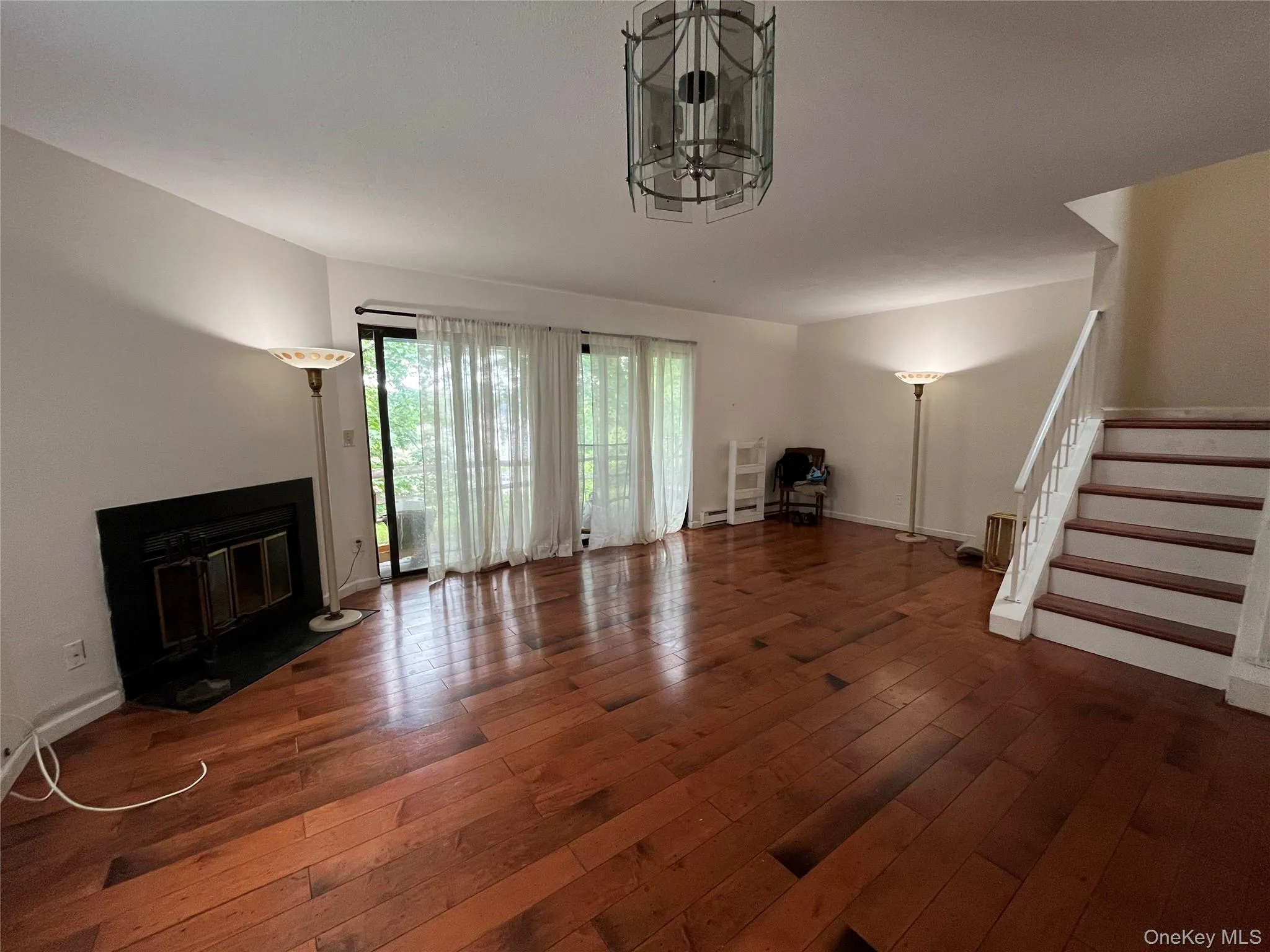 Unfurnished living room with wood-type flooring, stairs, a chandelier, and baseboard heating Unfurnished living room with wood-type flooring, stairs, a chandelier, and baseboard heating