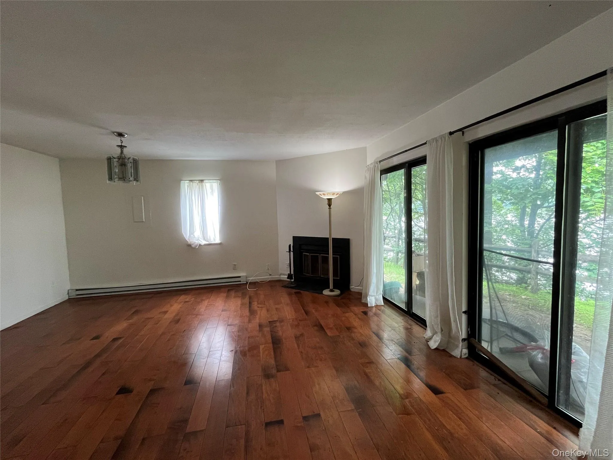 Unfurnished living room featuring a baseboard heating unit, a glass covered fireplace, and dark wood-style flooring Unfurnished living room featuring a baseboard heating unit, a glass covered fireplace, and dark wood-style flooring