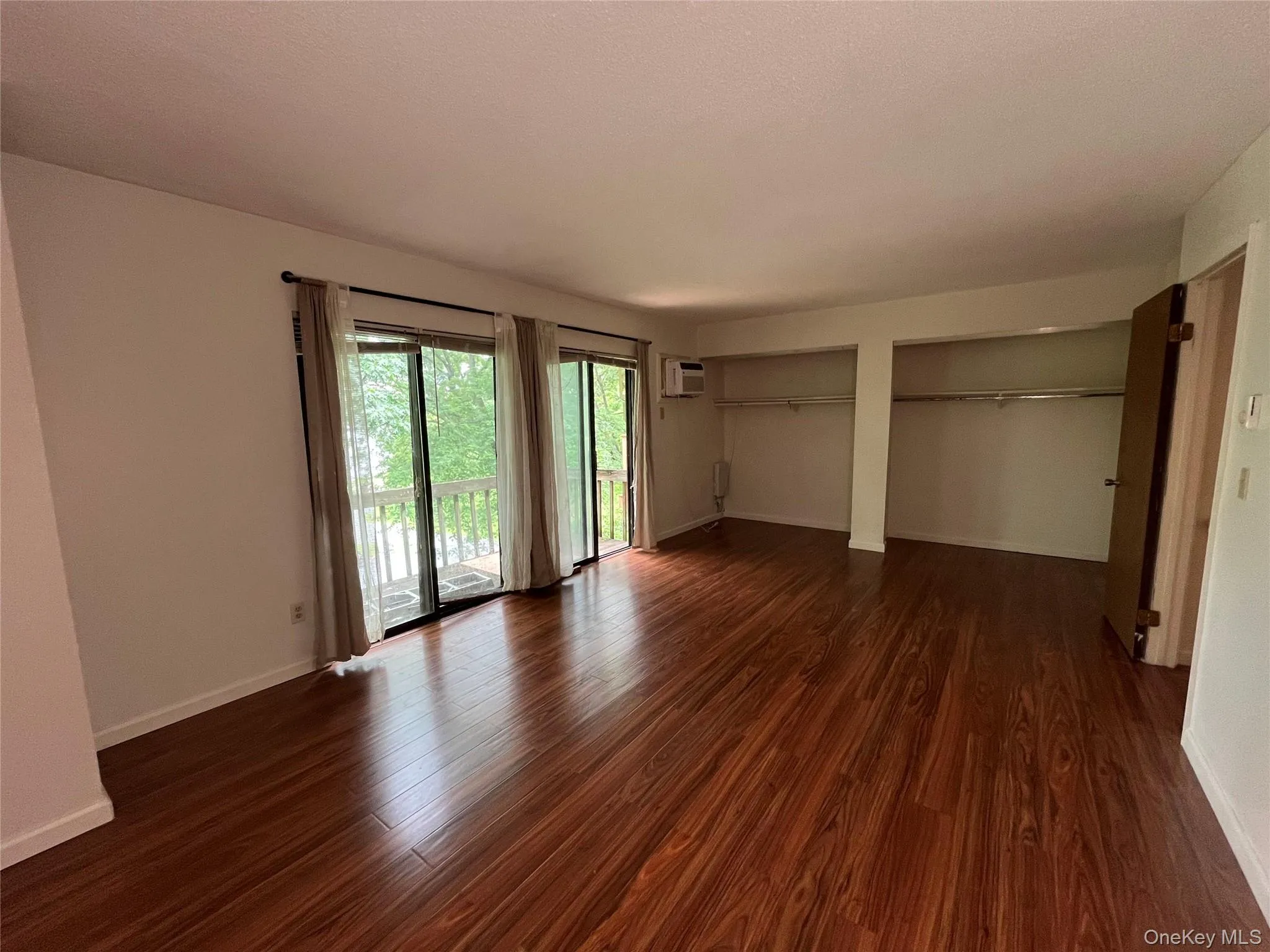 Unfurnished bedroom with access to exterior, dark wood-type flooring, multiple closets, and a wall mounted AC Unfurnished bedroom with access to exterior, dark wood-type flooring, multiple closets, and a wall mounted AC