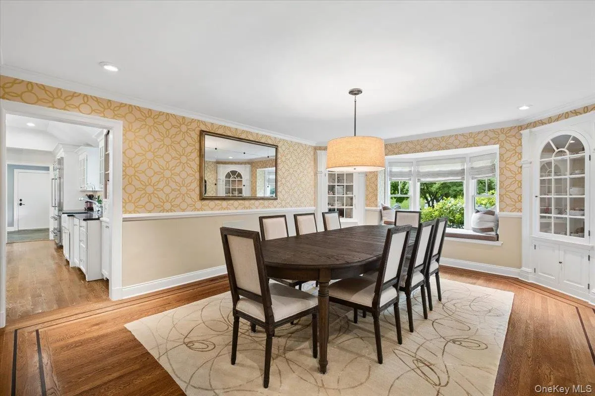 Dining area featuring hardwood flooring with inlay details, a built-in corner cabinet with glass doors, a bay window with a window seat, and easy entry to the gourmet kitchen Dining area featuring hardwood flooring with inlay details, a built-in corner cabinet with glass doors, a bay window with a window seat, and easy entry to the gourmet kitchen
