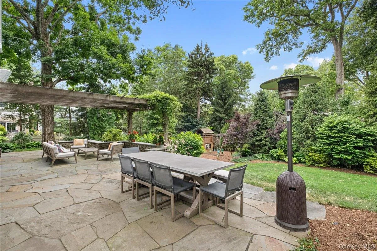 Welcoming flagstone patio featuring a wooden pergola, lush landscaping, and a lush green lawn surrounded by mature trees and bushes Welcoming flagstone patio featuring a wooden pergola, lush landscaping, and a lush green lawn surrounded by mature trees and bushes