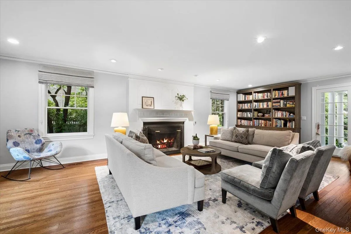 Spacious living area featuring hardwood flooring, a wood burning fireplace with a beautiful white mantel, a built-in bookcase and recessed lighting Spacious living area featuring hardwood flooring, a wood burning fireplace with a beautiful white mantel, a built-in bookcase and recessed lighting