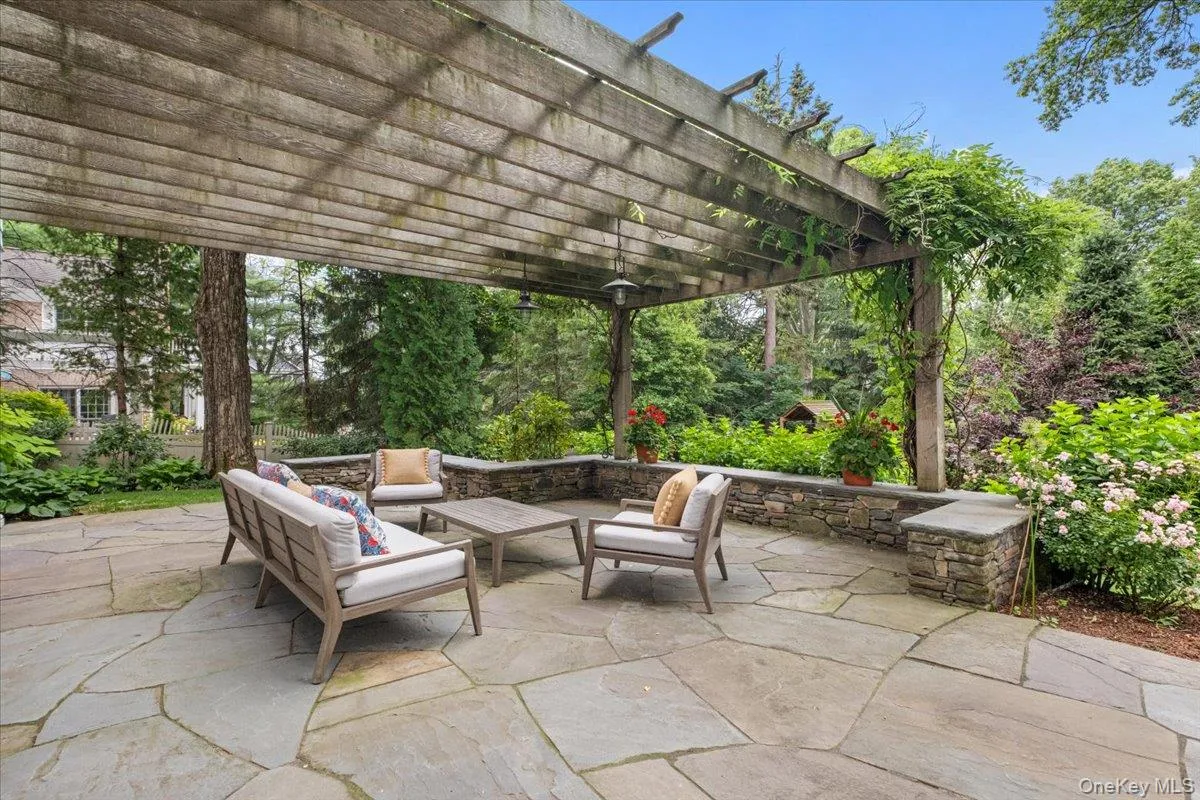Flagstone patio featuring a wooden pergola with climbing greenery, stone seating wall, and mature landscaping Flagstone patio featuring a wooden pergola with climbing greenery, stone seating wall, and mature landscaping