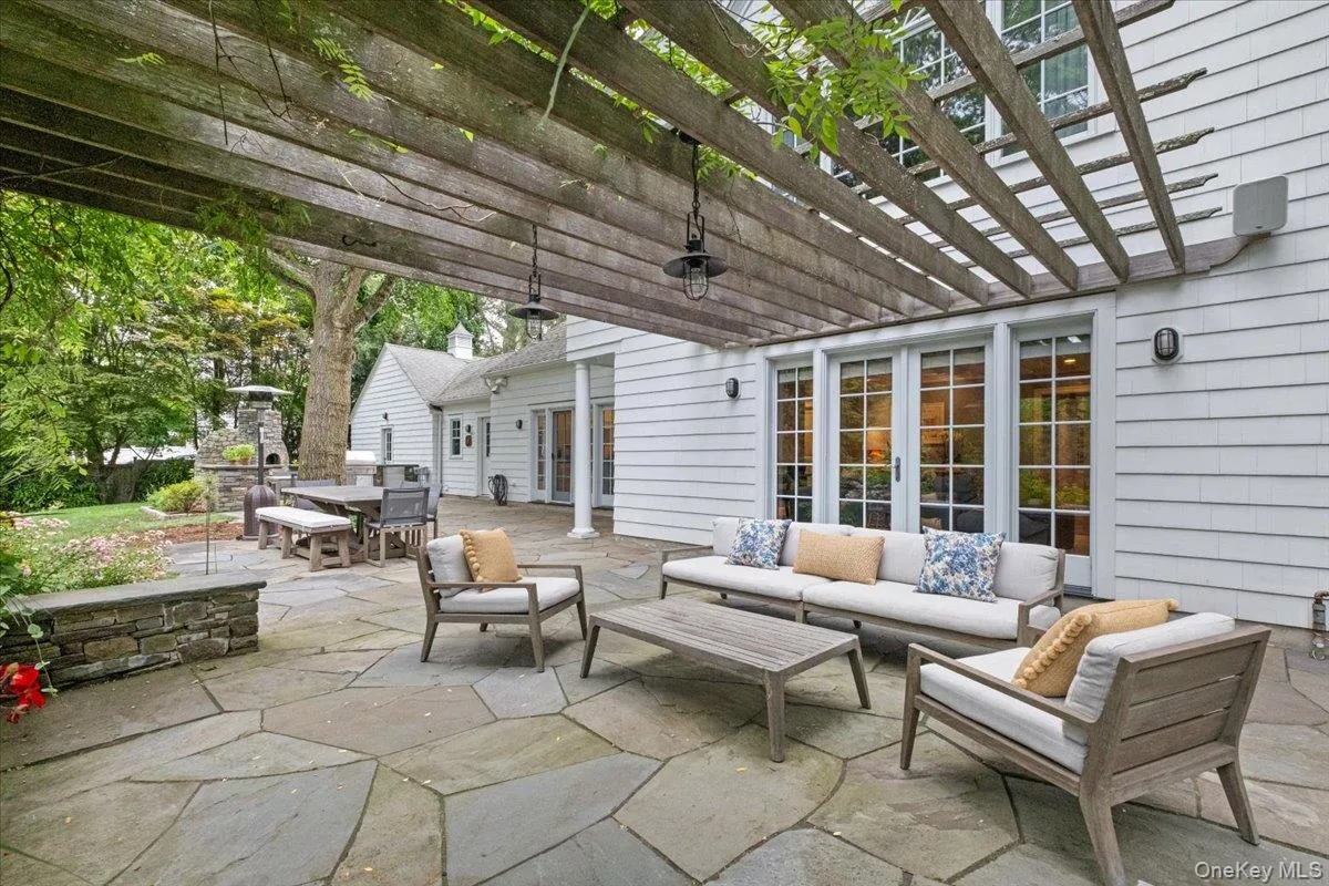 Expansive flagstone patio beneath a wooden pergola, featuring multiple sets of French doors creating easy access inside and out, beautiful plantings and a stone outdoor oven ready for your parties Expansive flagstone patio beneath a wooden pergola, featuring multiple sets of French doors creating easy access inside and out, beautiful plantings and a stone outdoor oven ready for your parties
