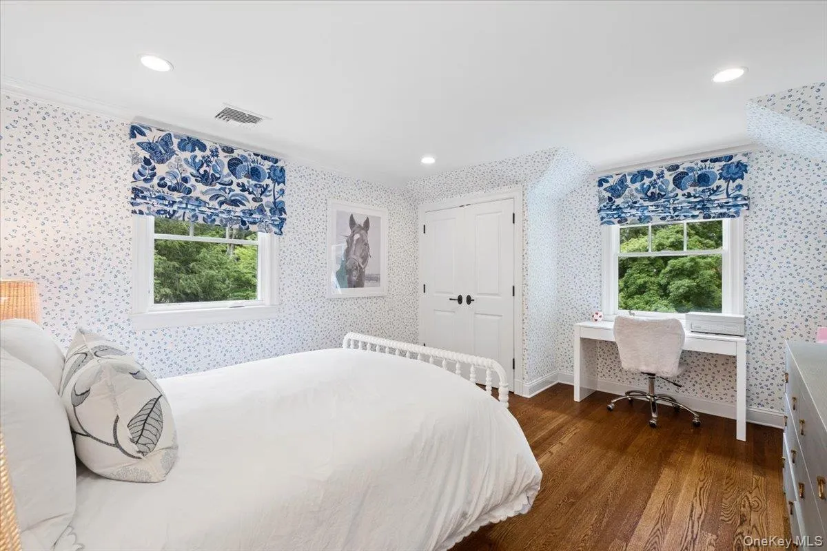 Bedroom featuring hardwood flooring, white trim, recessed lighting, and dual white windows with patterned Roman shades Bedroom featuring hardwood flooring, white trim, recessed lighting, and dual white windows with patterned Roman shades