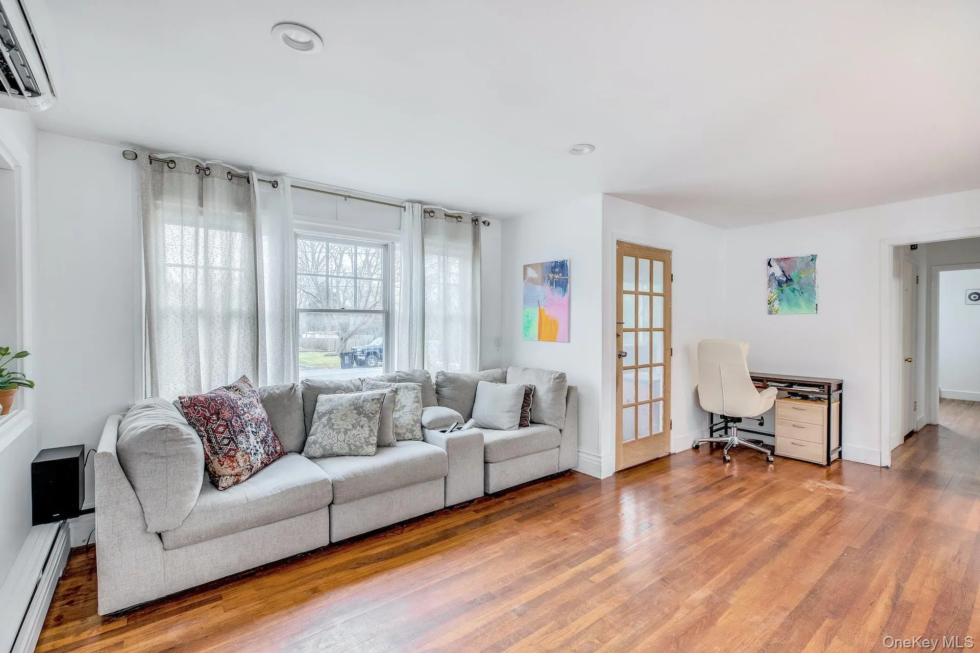 Spacious living area featuring rich hardwood flooring, crisp white walls, recessed ceiling lighting, and large windows with privacy treatments Spacious living area featuring rich hardwood flooring, crisp white walls, recessed ceiling lighting, and large windows with privacy treatments