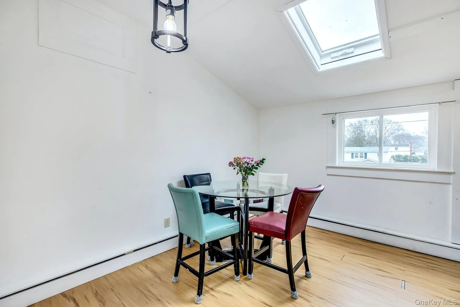 Room featuring wood-finish flooring, a prominent skylight, a large window, a vaulted ceiling, and a modern ceiling light fixture Room featuring wood-finish flooring, a prominent skylight, a large window, a vaulted ceiling, and a modern ceiling light fixture