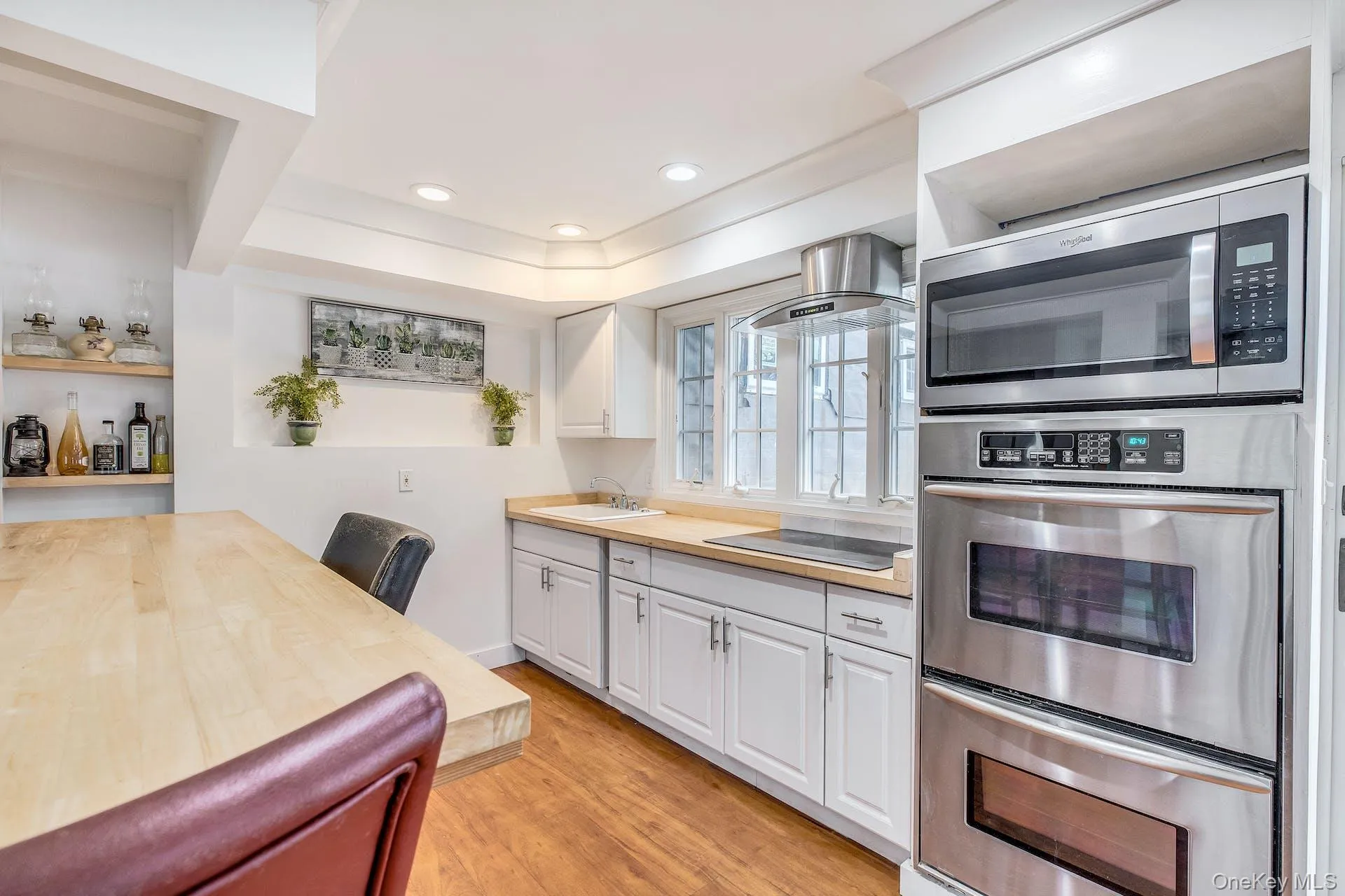 Kitchen featuring stainless steel built-in double oven and microwave, light wood-finish countertops, white cabinetry, and wood-finish flooring Kitchen featuring stainless steel built-in double oven and microwave, light wood-finish countertops, white cabinetry, and wood-finish flooring