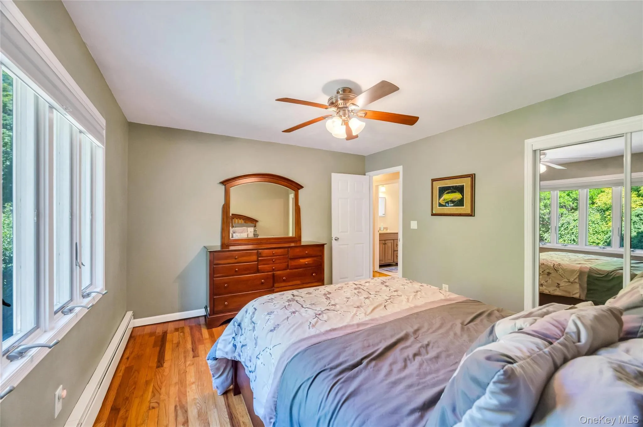 Bedroom featuring wood-finish flooring, a ceiling fan with integrated lighting, and multiple windows Bedroom featuring wood-finish flooring, a ceiling fan with integrated lighting, and multiple windows