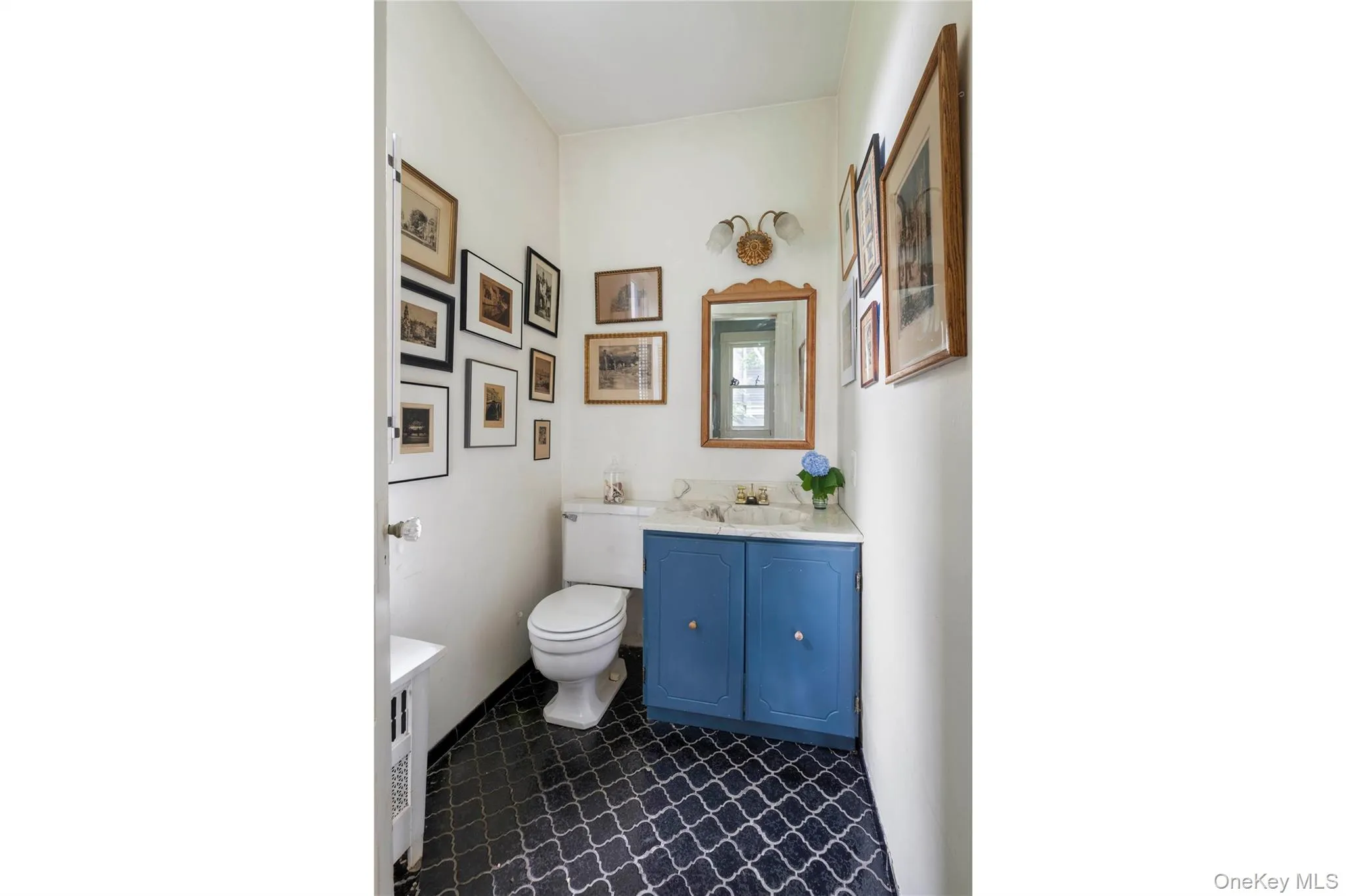 Powder room featuring a blue vanity with a white countertop, coordinating mirror with wall-mounted sconce lighting, and patterned floor tiling Powder room featuring a blue vanity with a white countertop, coordinating mirror with wall-mounted sconce lighting, and patterned floor tiling