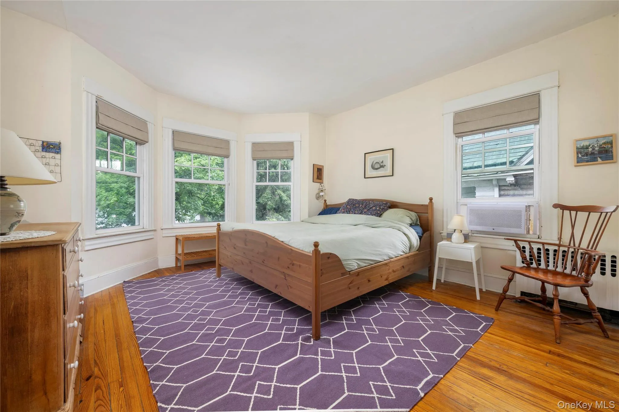 Bedroom with wood-finish flooring, a bay window with three double-hung windows, and light-colored walls Bedroom with wood-finish flooring, a bay window with three double-hung windows, and light-colored walls