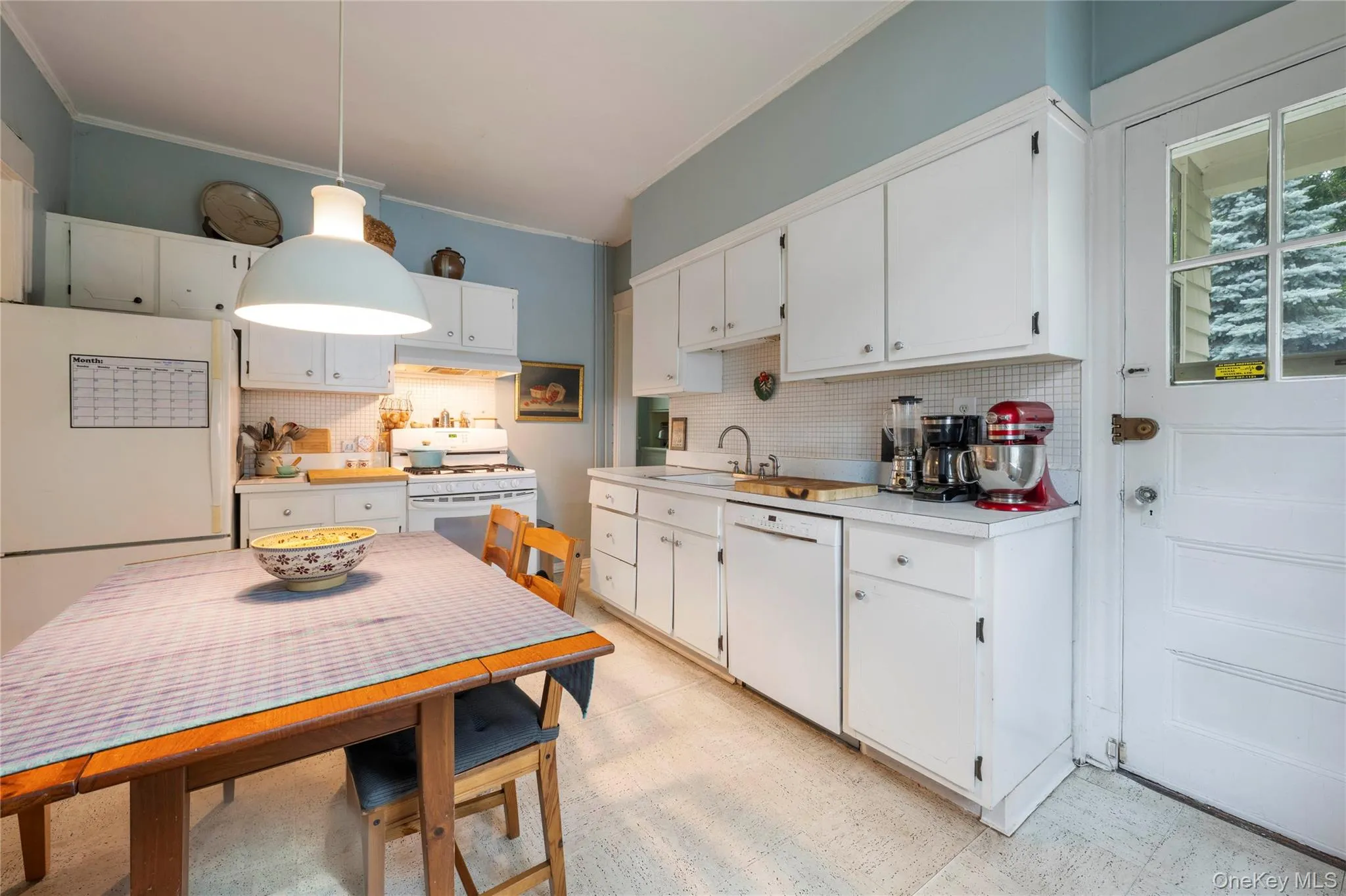 Bright kitchen featuring white cabinetry, a white tile backsplash, a built-in dishwasher, and a white refrigerator Bright kitchen featuring white cabinetry, a white tile backsplash, a built-in dishwasher, and a white refrigerator