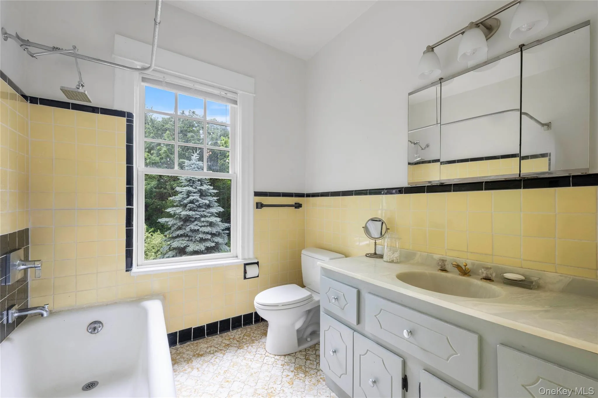 Bathroom featuring a window, yellow wall tiling with black trim, a bathtub with shower fixture, a toilet, and a vanity with an integrated sink and mirror cabinet Bathroom featuring a window, yellow wall tiling with black trim, a bathtub with shower fixture, a toilet, and a vanity with an integrated sink and mirror cabinet