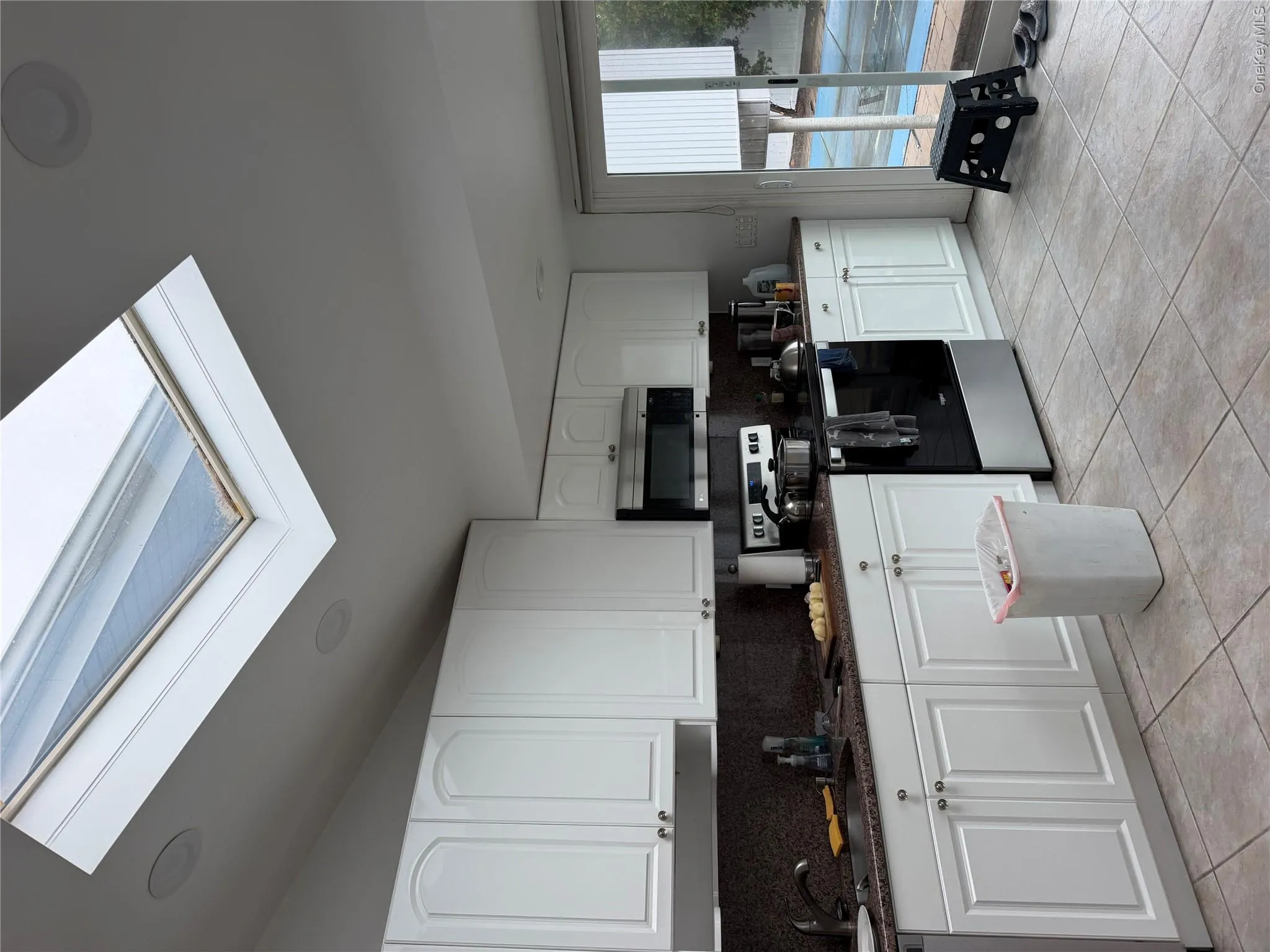Kitchen featuring a vaulted ceiling with skylight, recessed lighting, white cabinetry, dark speckled countertops, and tile flooring Kitchen featuring a vaulted ceiling with skylight, recessed lighting, white cabinetry, dark speckled countertops, and tile flooring