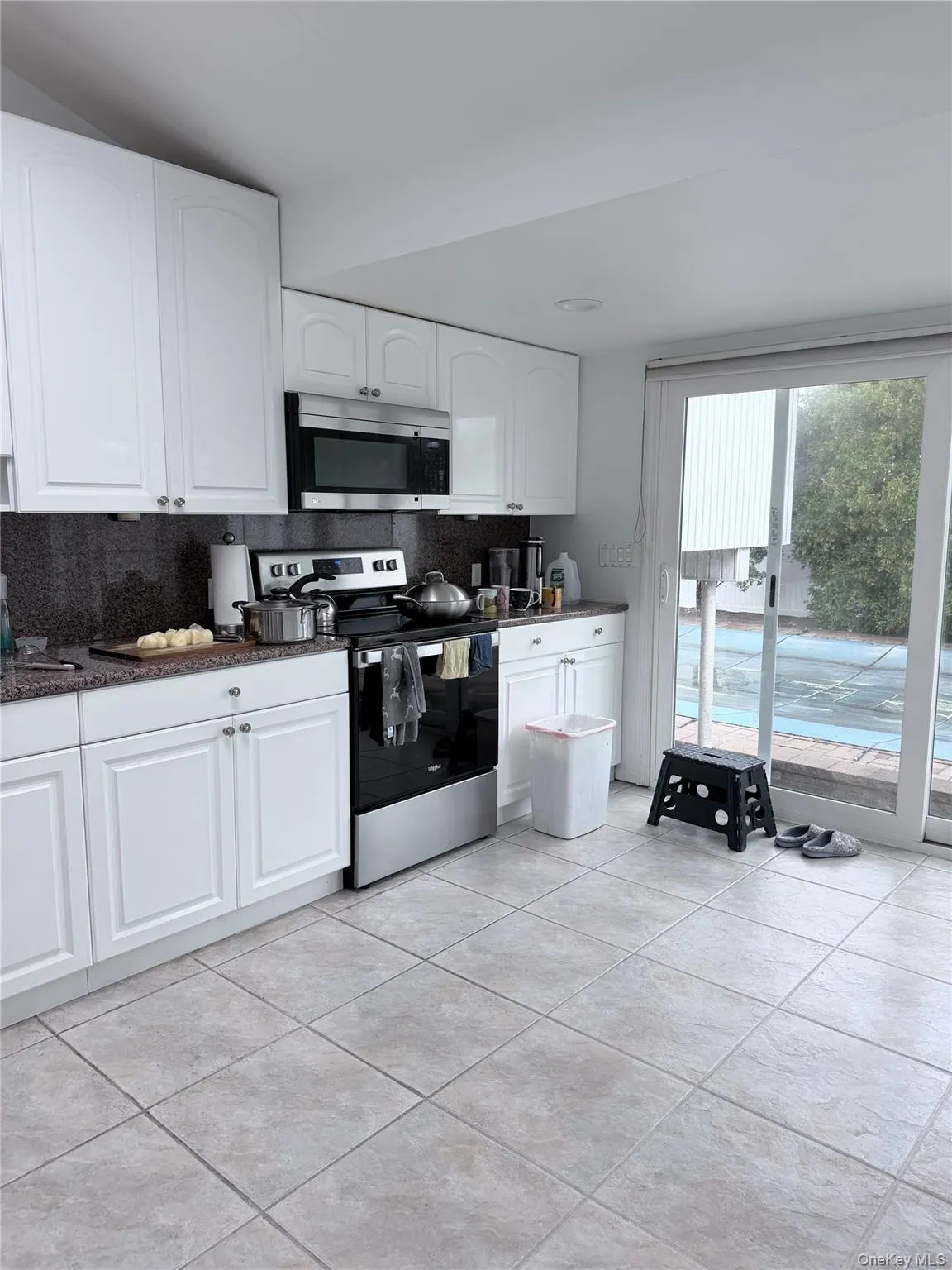 Kitchen featuring white cabinetry, dark countertops, a stainless steel range, and tile flooring Kitchen featuring white cabinetry, dark countertops, a stainless steel range, and tile flooring