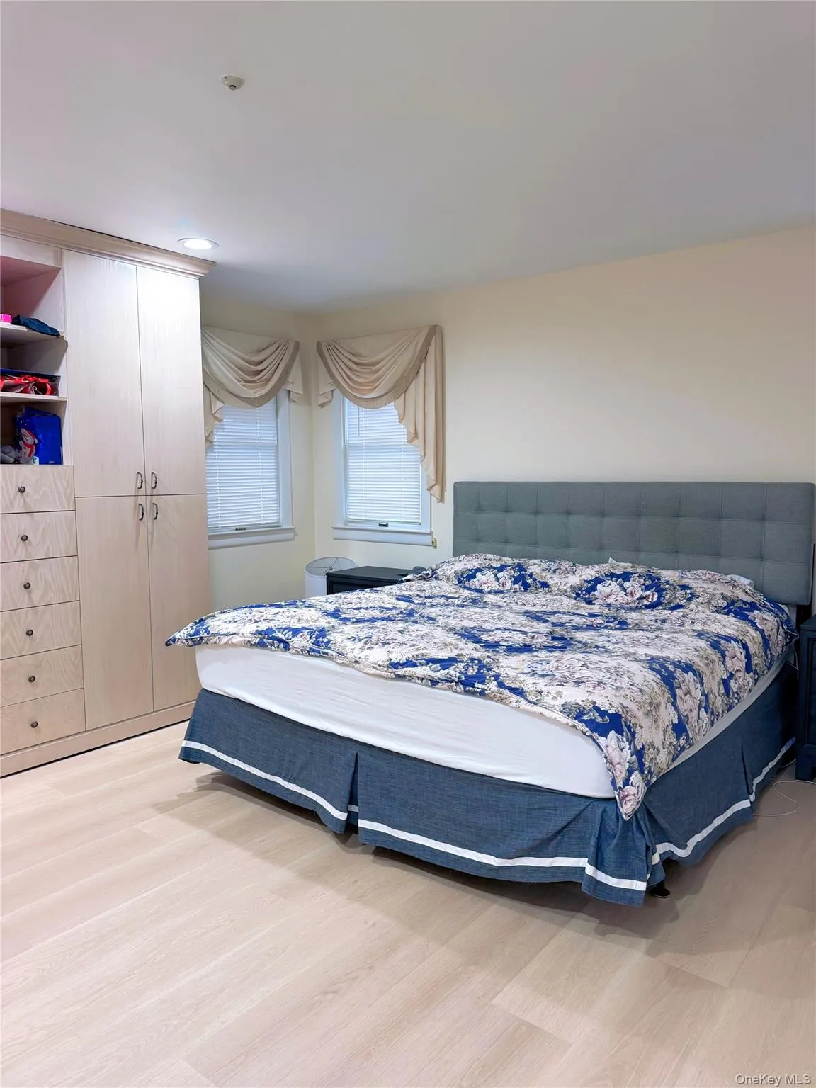 Spacious room featuring light wood-finish flooring, built-in cabinetry with drawers and wardrobes, two windows with window treatments, and recessed lighting Spacious room featuring light wood-finish flooring, built-in cabinetry with drawers and wardrobes, two windows with window treatments, and recessed lighting