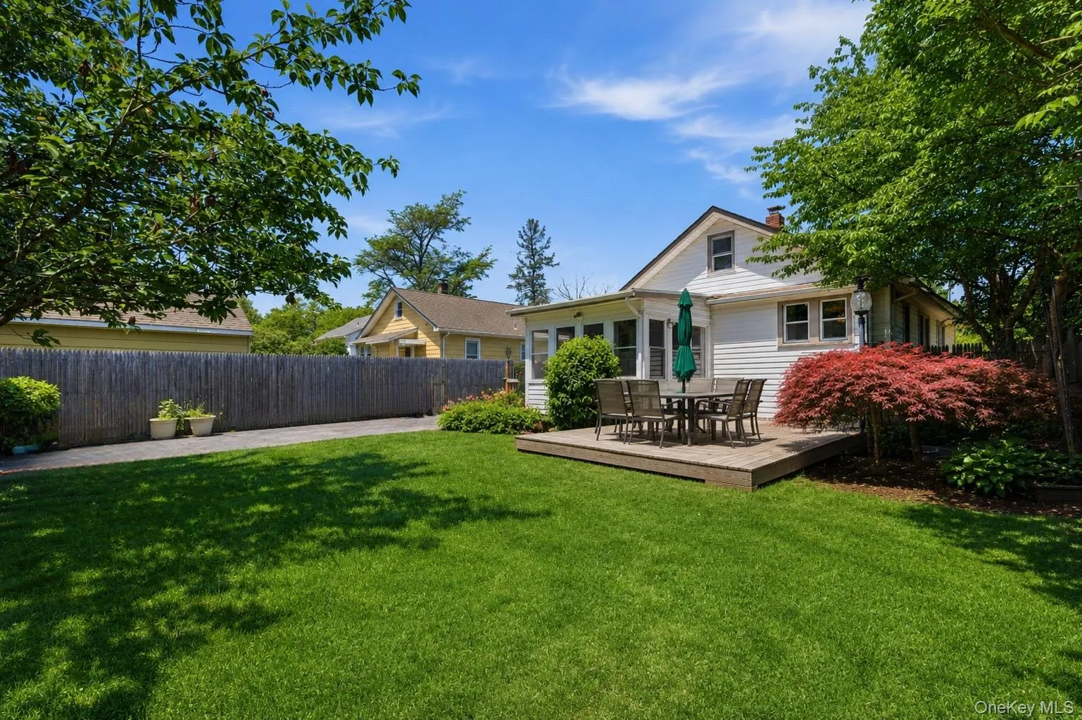 Expansive backyard featuring a lush lawn, a wood-finish deck, and mature landscaping Expansive backyard featuring a lush lawn, a wood-finish deck, and mature landscaping