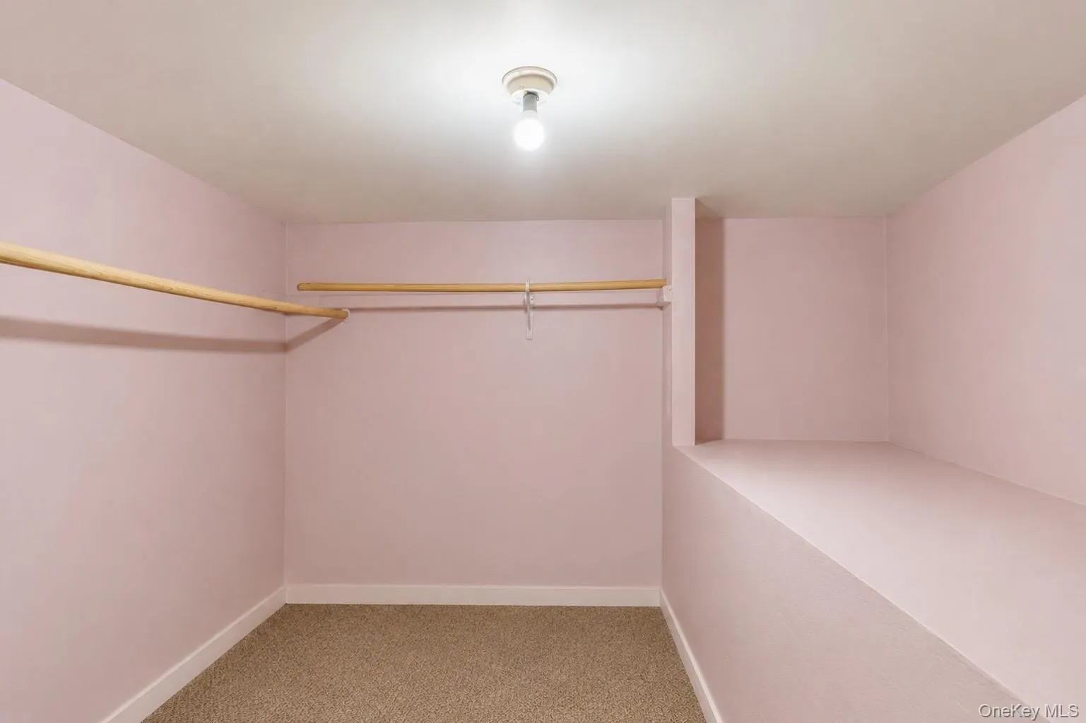 Carpeted closet space featuring a built-in shelf, two wooden clothing rods, and a ceiling-mounted light fixture Carpeted closet space featuring a built-in shelf, two wooden clothing rods, and a ceiling-mounted light fixture