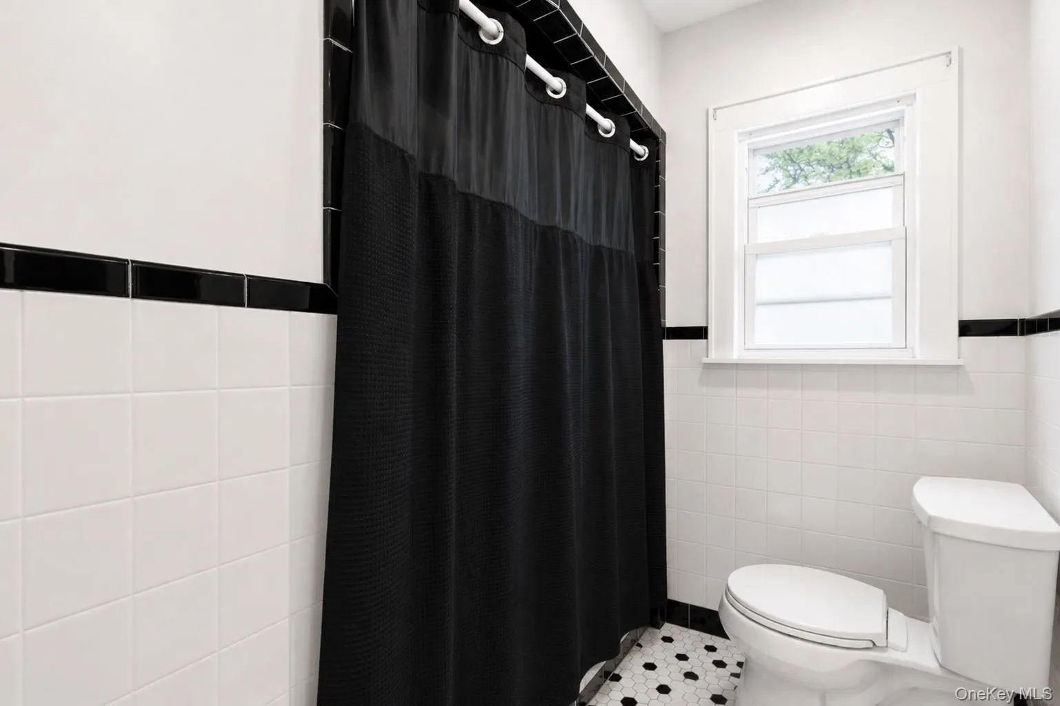 Bathroom featuring white subway tile walls with black trim, a toilet, a single window, and hexagonal floor tiling Bathroom featuring white subway tile walls with black trim, a toilet, a single window, and hexagonal floor tiling